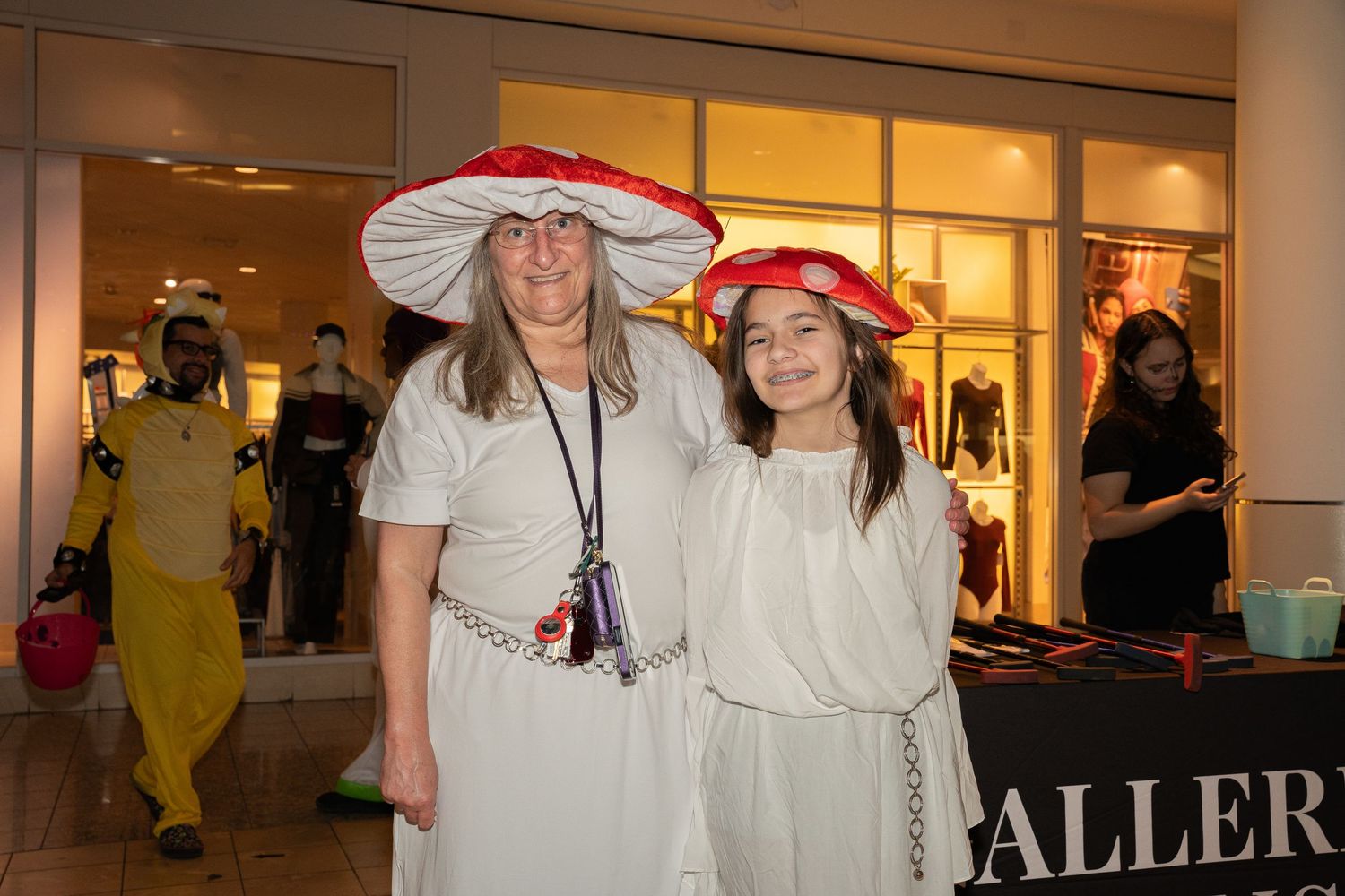 Two people wearing matching white outfits and red floppy hats pose together at an indoor event.
