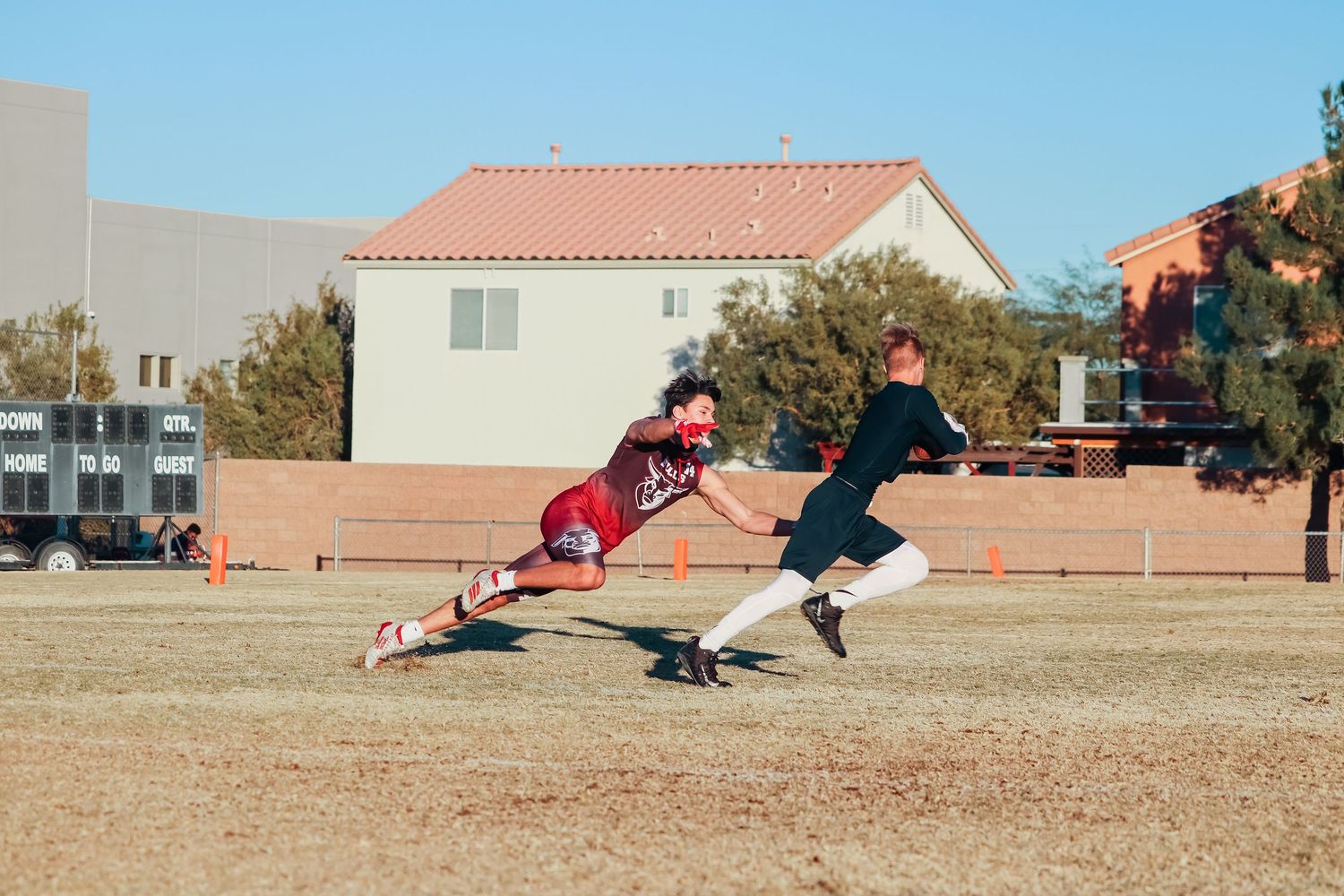 Two players engage in a flag football play with one diving to grab the flag.