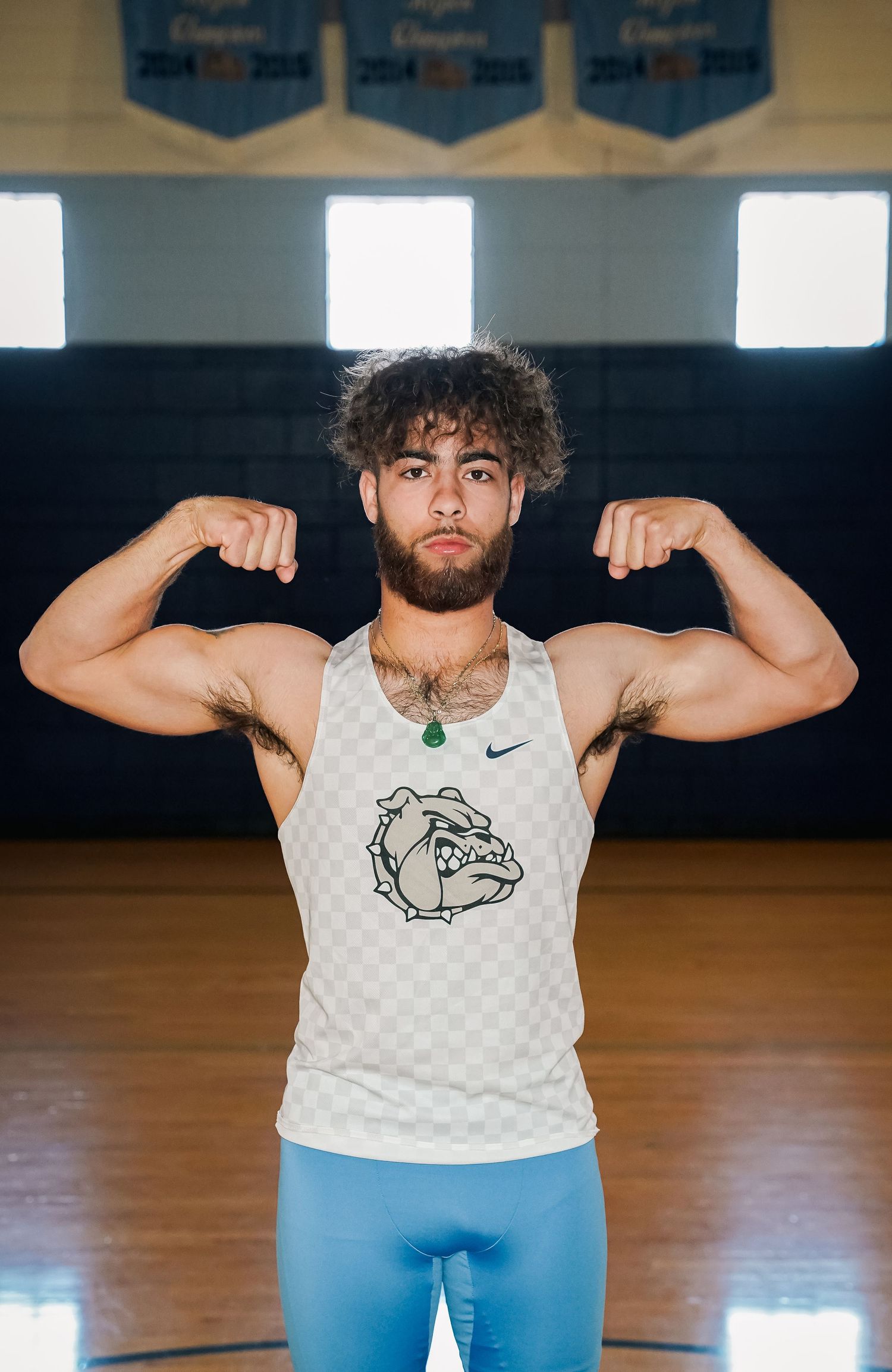 Athlete in white tank top flexes muscles while posing in indoor gymnasium setting.