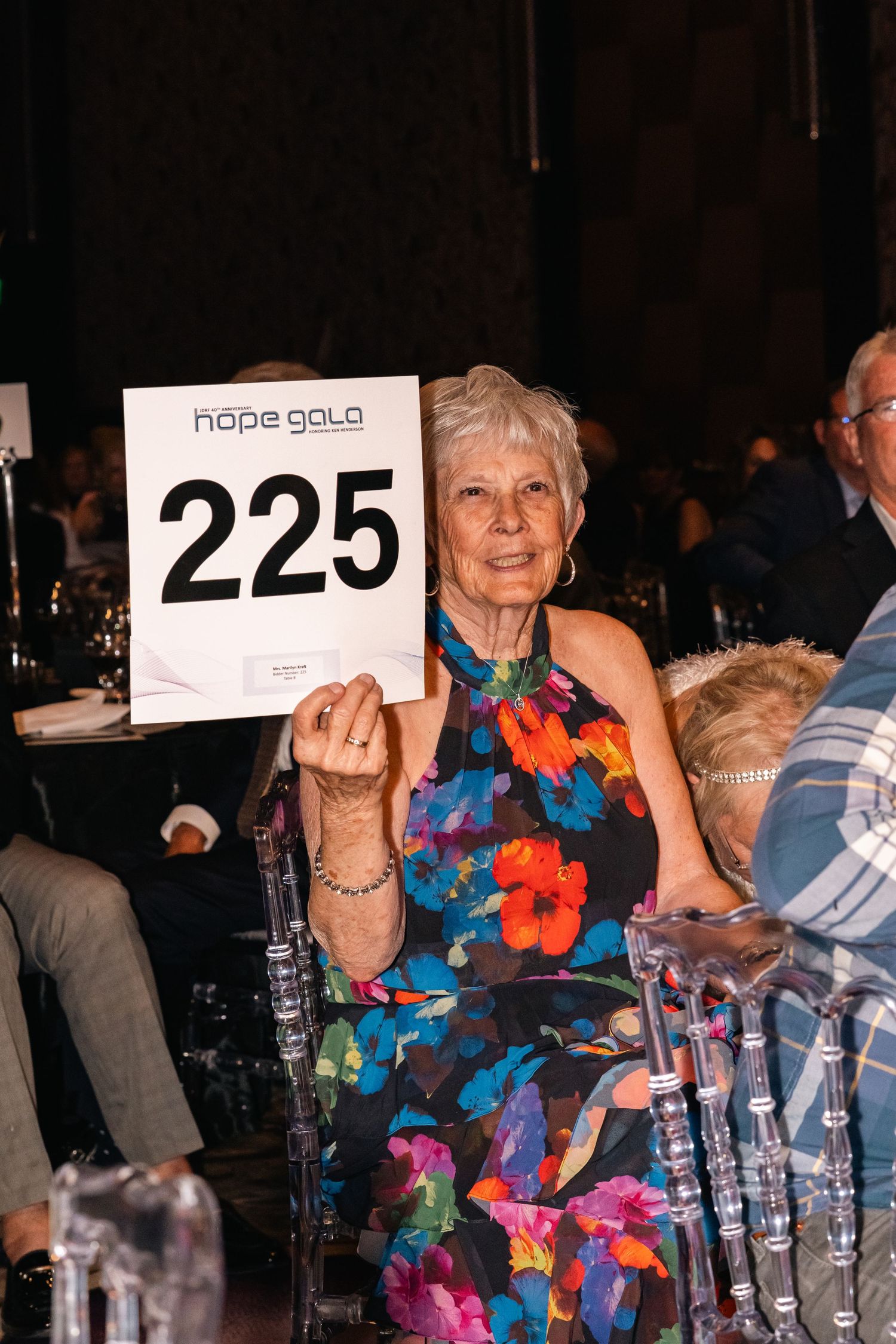 Person holding up auction paddle number 225 at formal gala event.