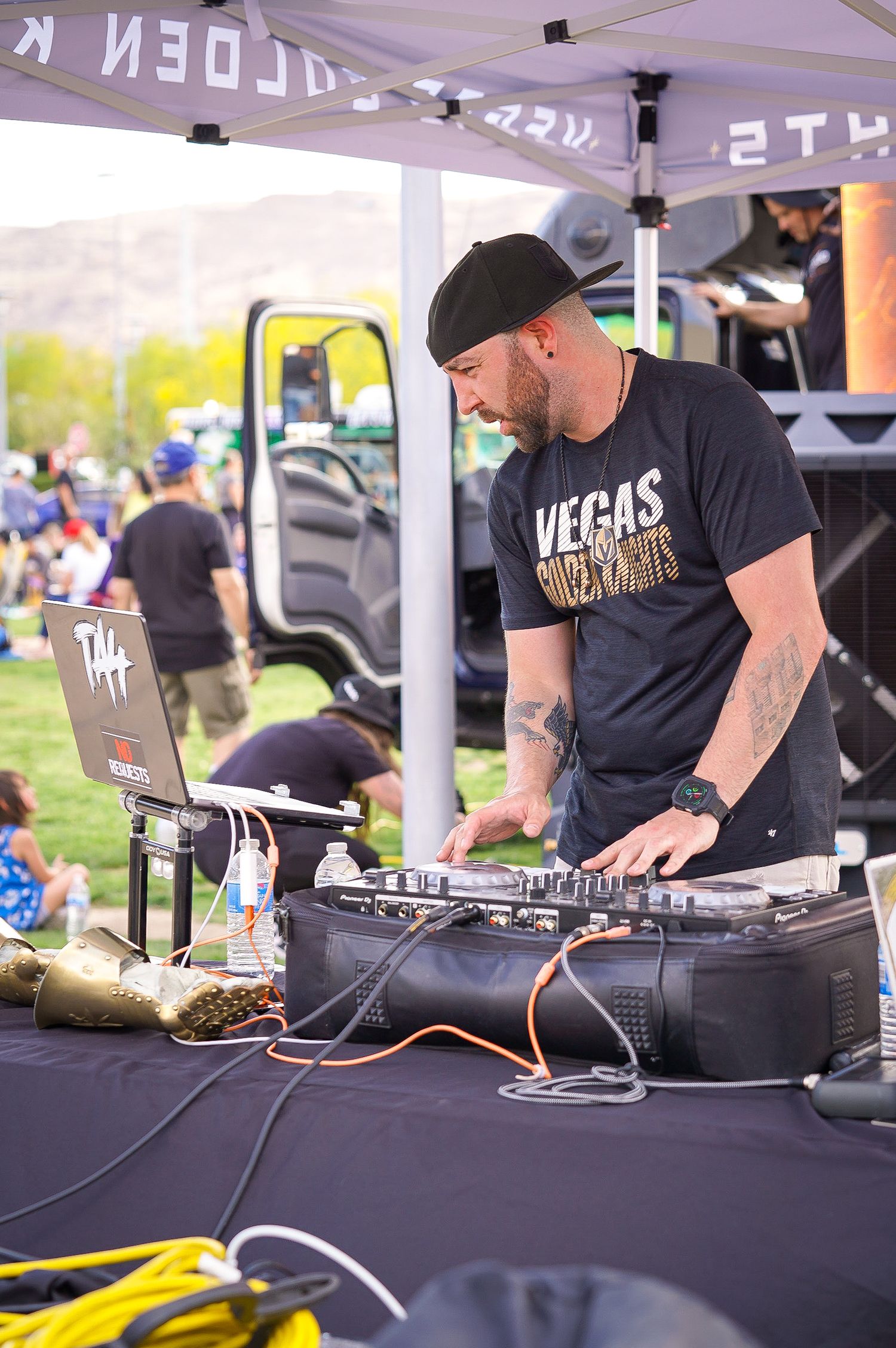 DJ performs at outdoor event wearing Vegas Golden Knights merchandise behind professional mixing equipment.