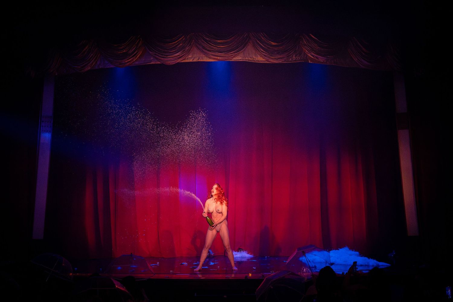 Solo performer on stage illuminated by red spotlight against dark theater curtains.