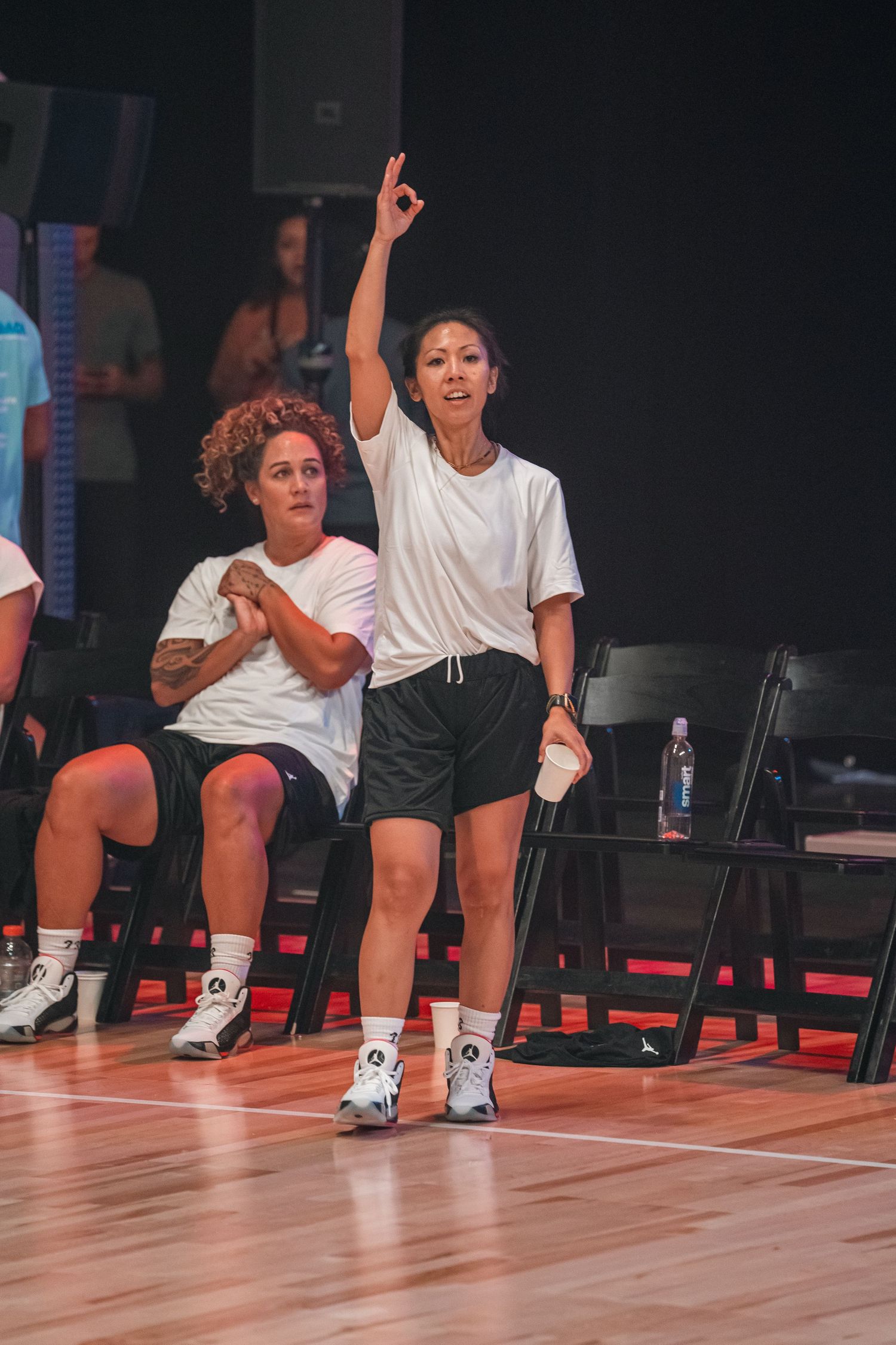 Athletes in white shirts and black shorts practicing on a wooden indoor court.