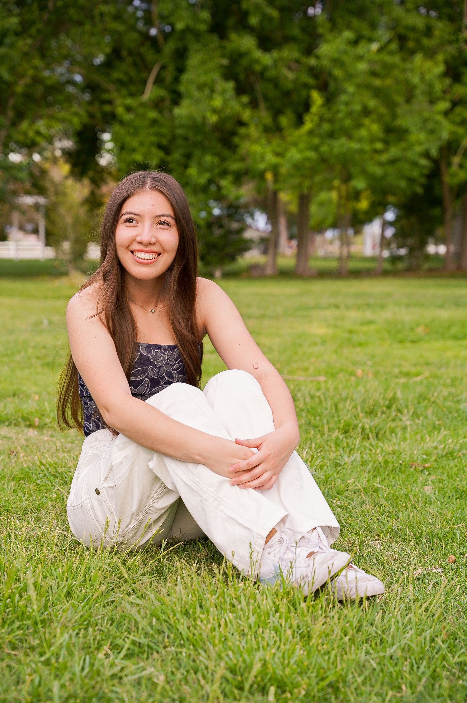 Student relaxes on grass wearing casual outfit in sunny park setting.