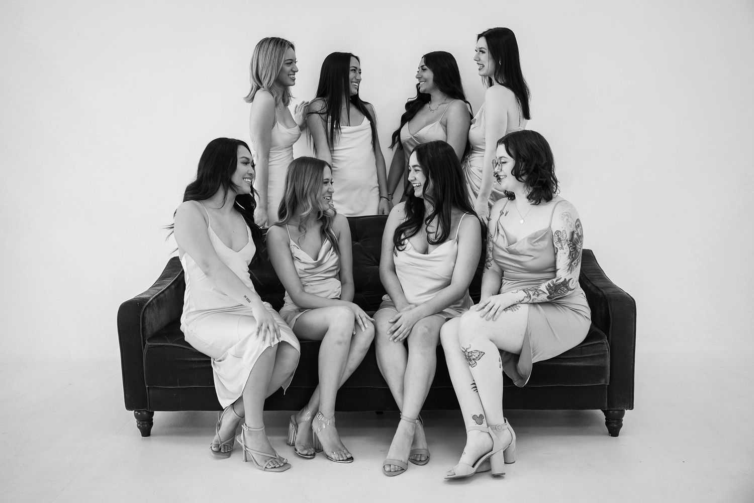Group gathered on a black couch in casual white outfits for a studio photoshoot.