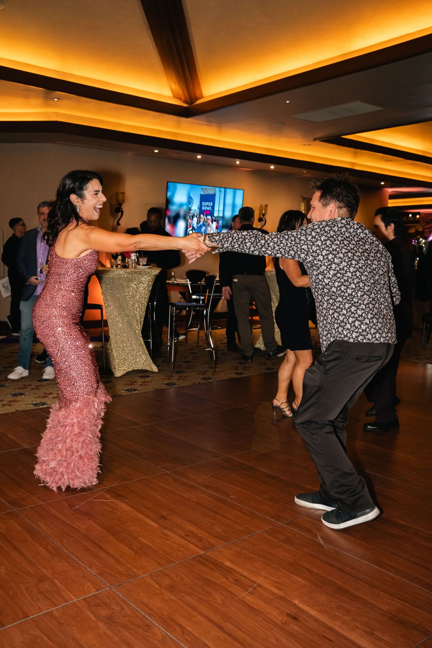 Couple dancing energetically on wooden dance floor at formal event.