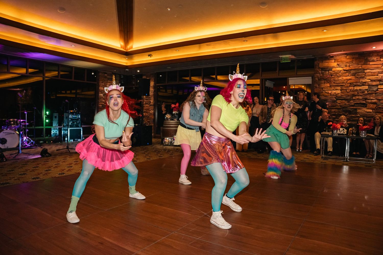 Dancers in colorful tutus and unicorn headbands perform on a wooden dance floor at a party.