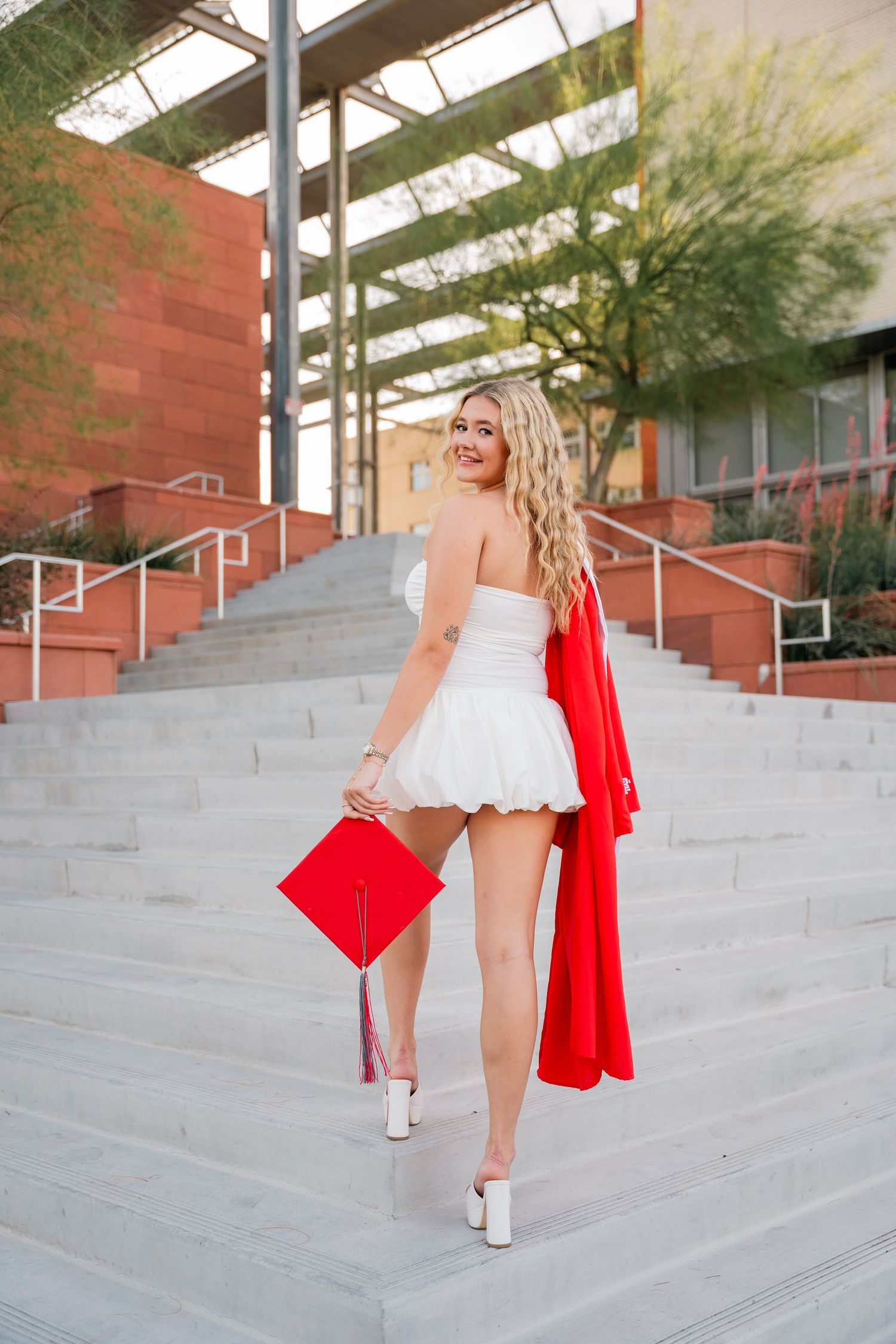 Graduate walks up concrete stairs in red gown and white dress.
