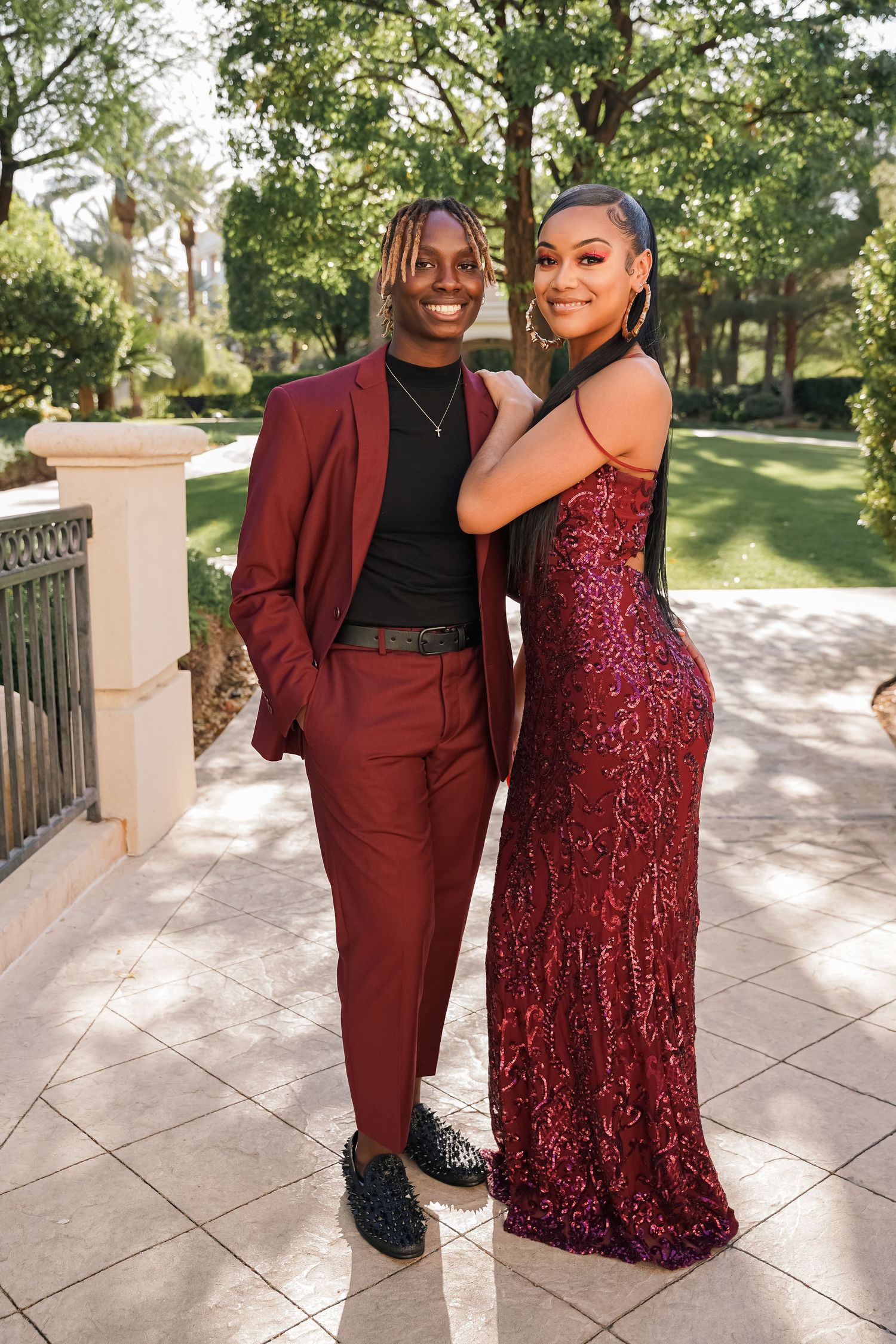 Couple in coordinating burgundy formal wear pose together on outdoor terrace.