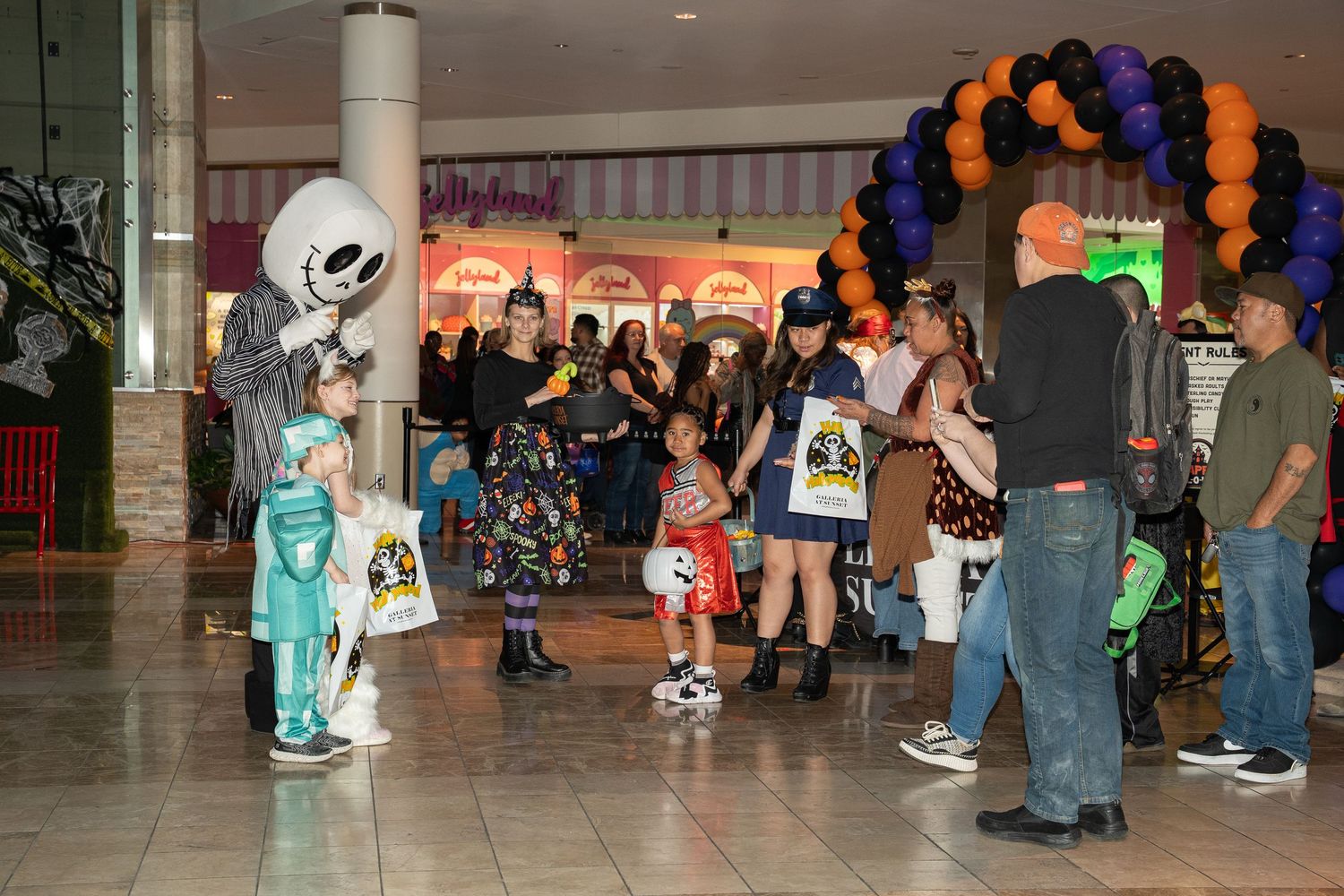 Halloween celebration with balloon arch decorations and costumed attendees in a mall setting.