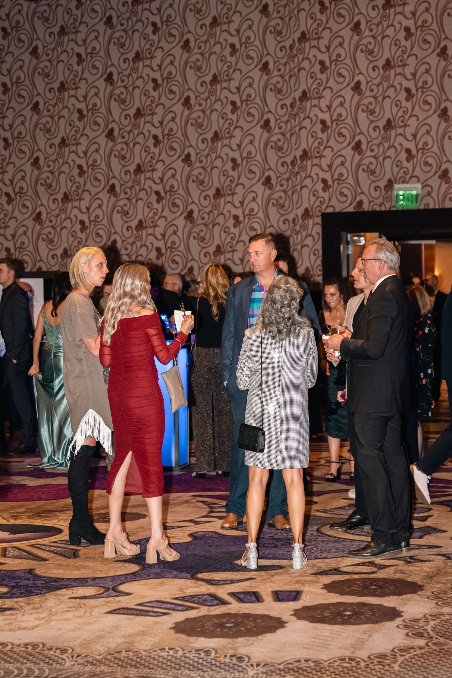 Group of guests in formal attire socializing during an evening gala event.