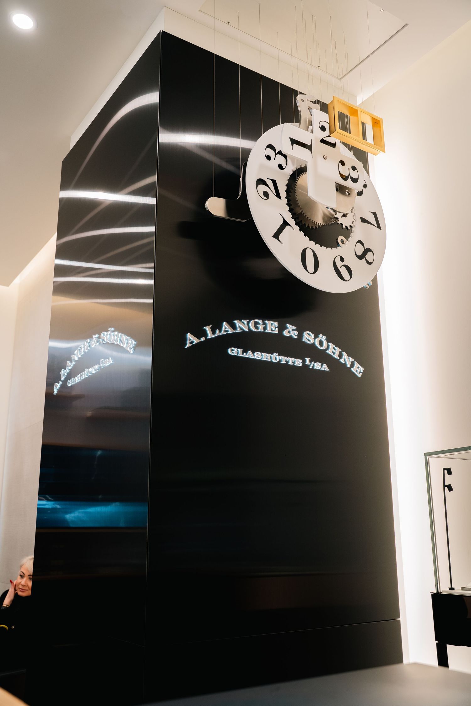 Large A. Lange & Sohne brand clock display mounted on a black wall with LED lighting.