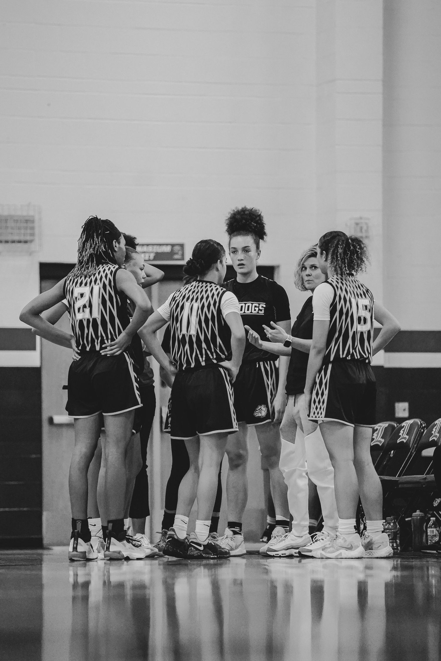 Basketball team huddles together on court during practice in black and white uniforms.