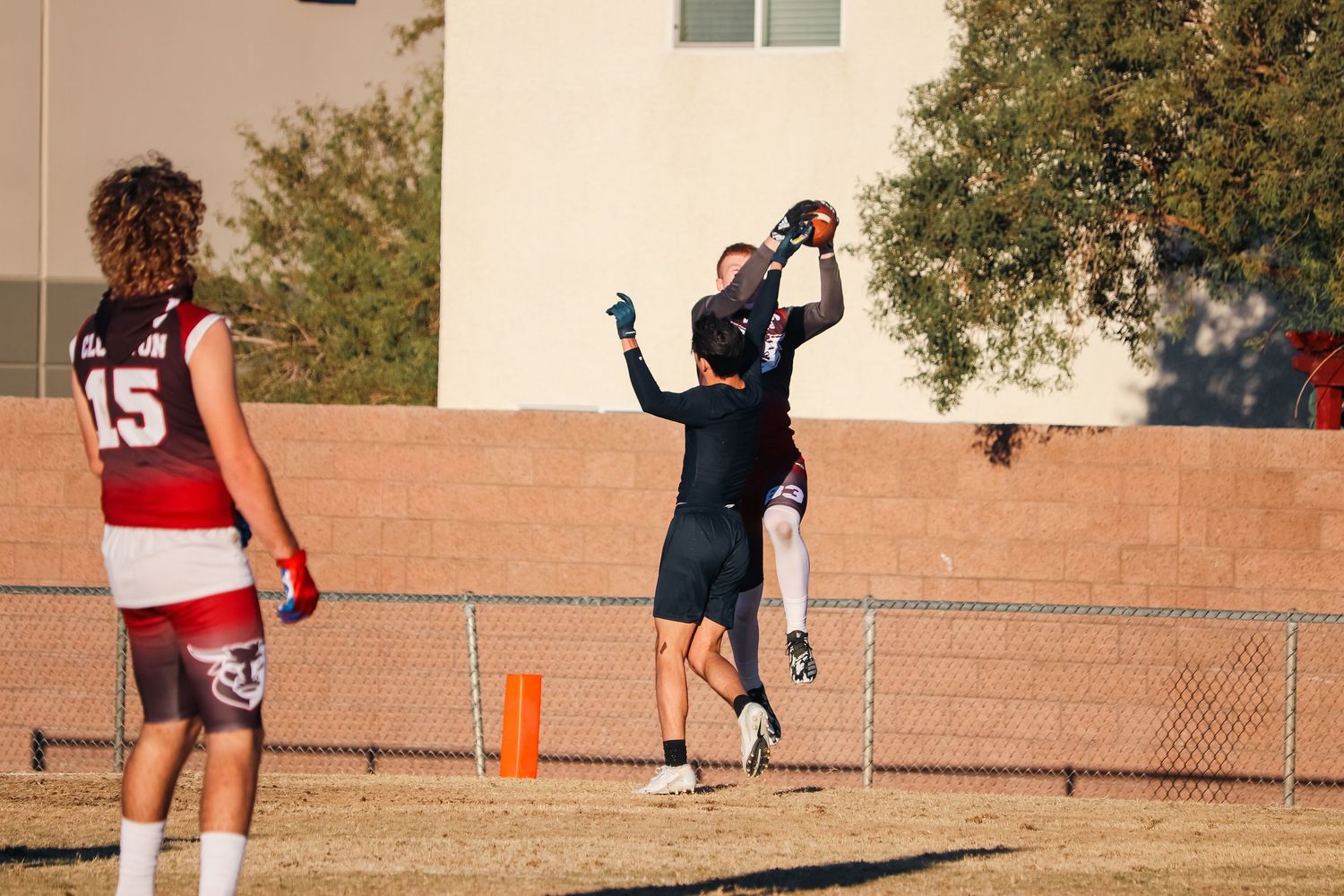 Athlete jumps high to catch football during outdoor game with other players nearby.