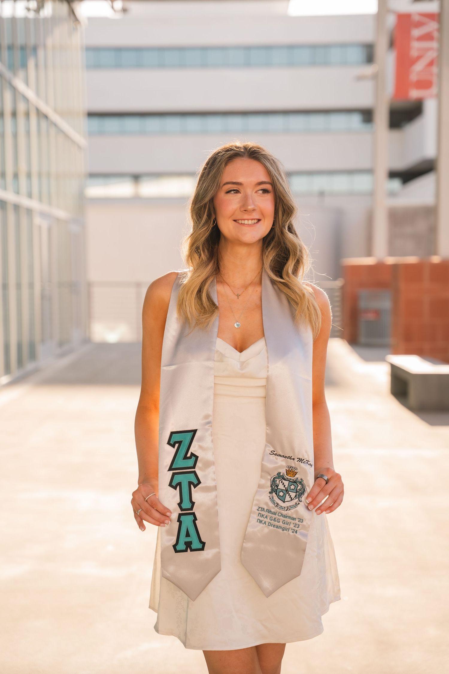 Graduate wearing white dress and sorority stole poses on UNLV campus.