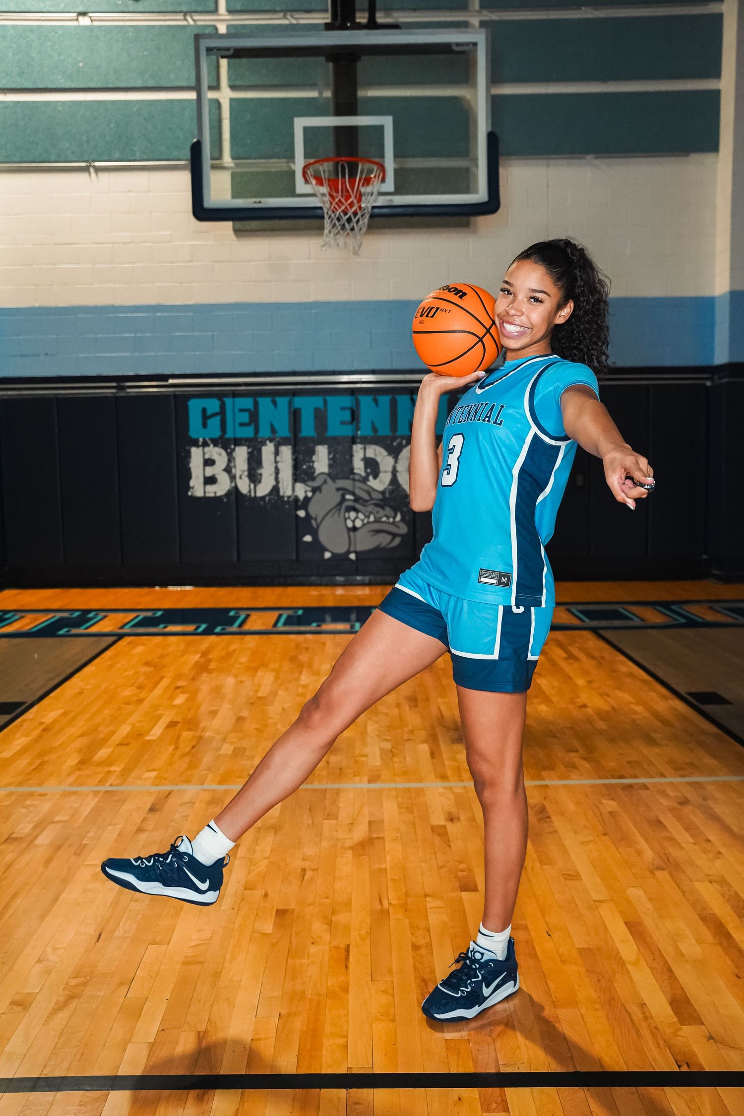 Player in light blue uniform performs dynamic basketball dribbling moves on wooden court floor.