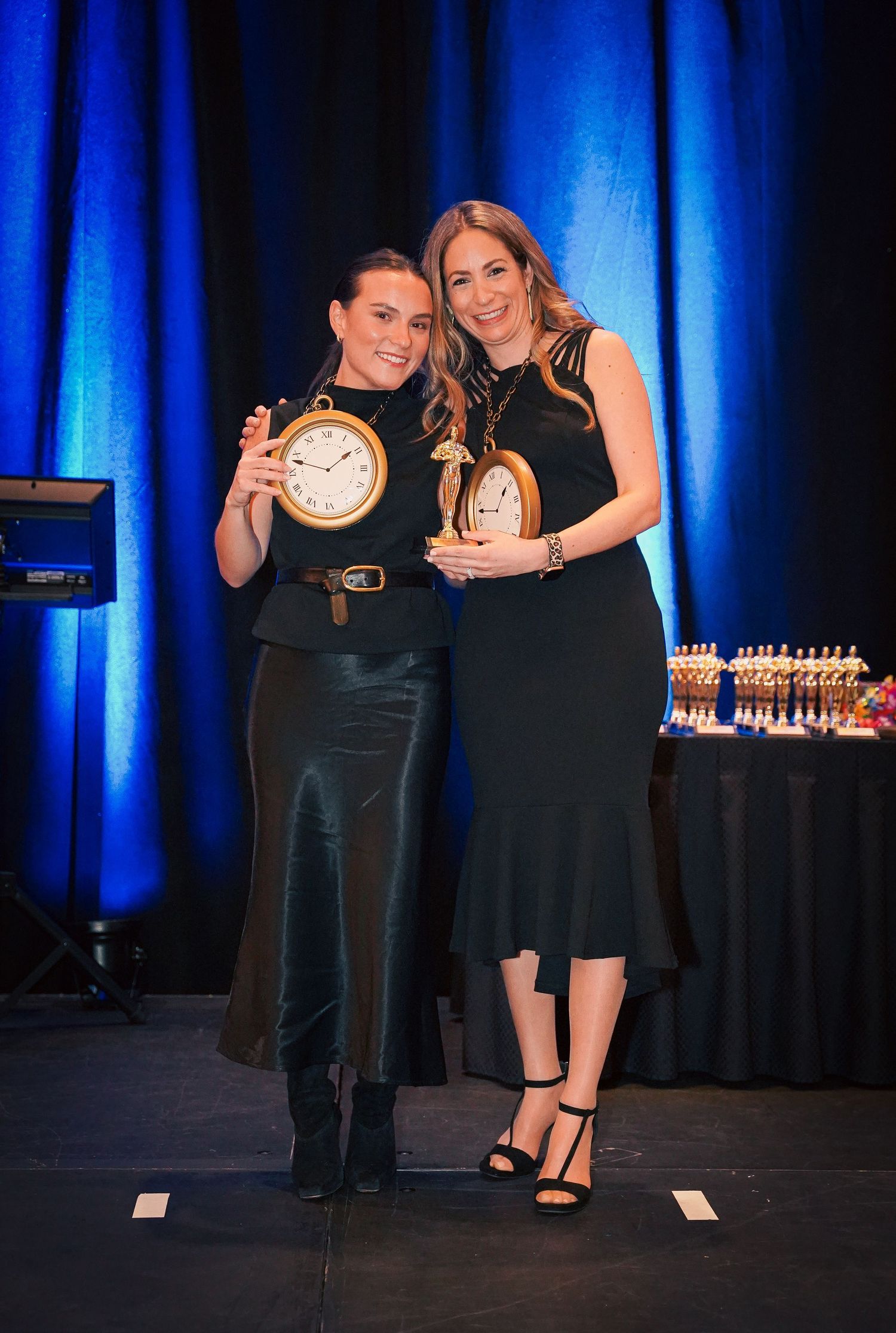 Two award recipients pose with trophies against a blue-lit backdrop at an elegant ceremony event.