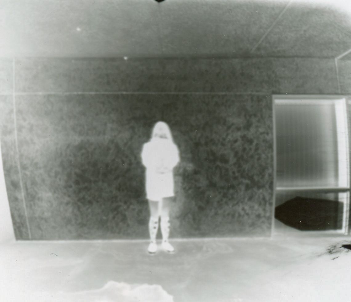 Black and white photo of a solitary figure standing in a dark room.