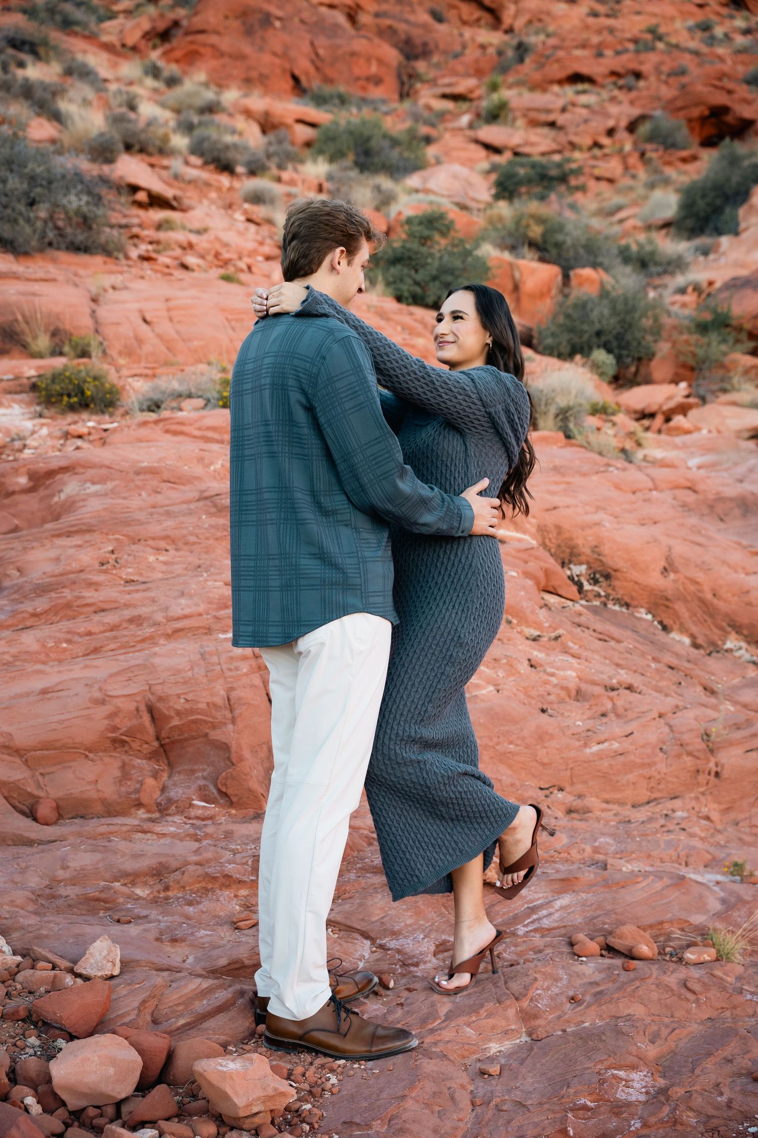 A romantic embrace between a couple on red rock formations at sunset.