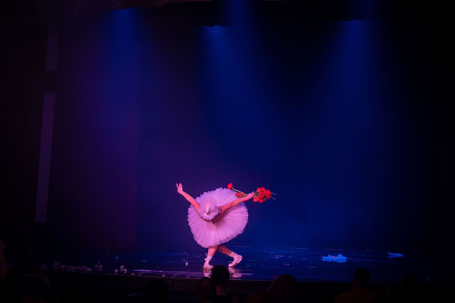 A whimsical performer in a pink costume dances under blue stage lighting.