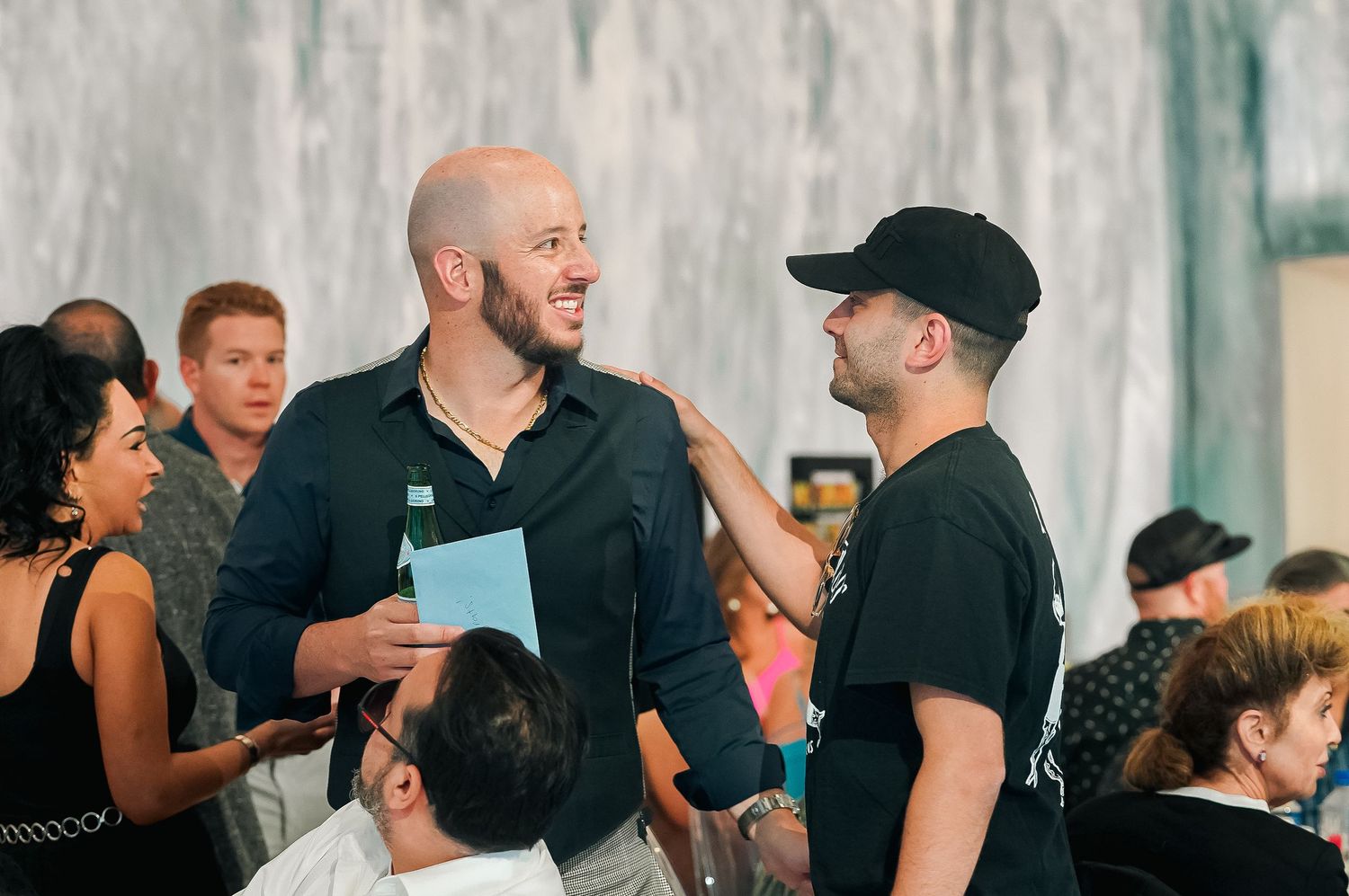 Three people engaged in conversation at an indoor event with gray textured walls.