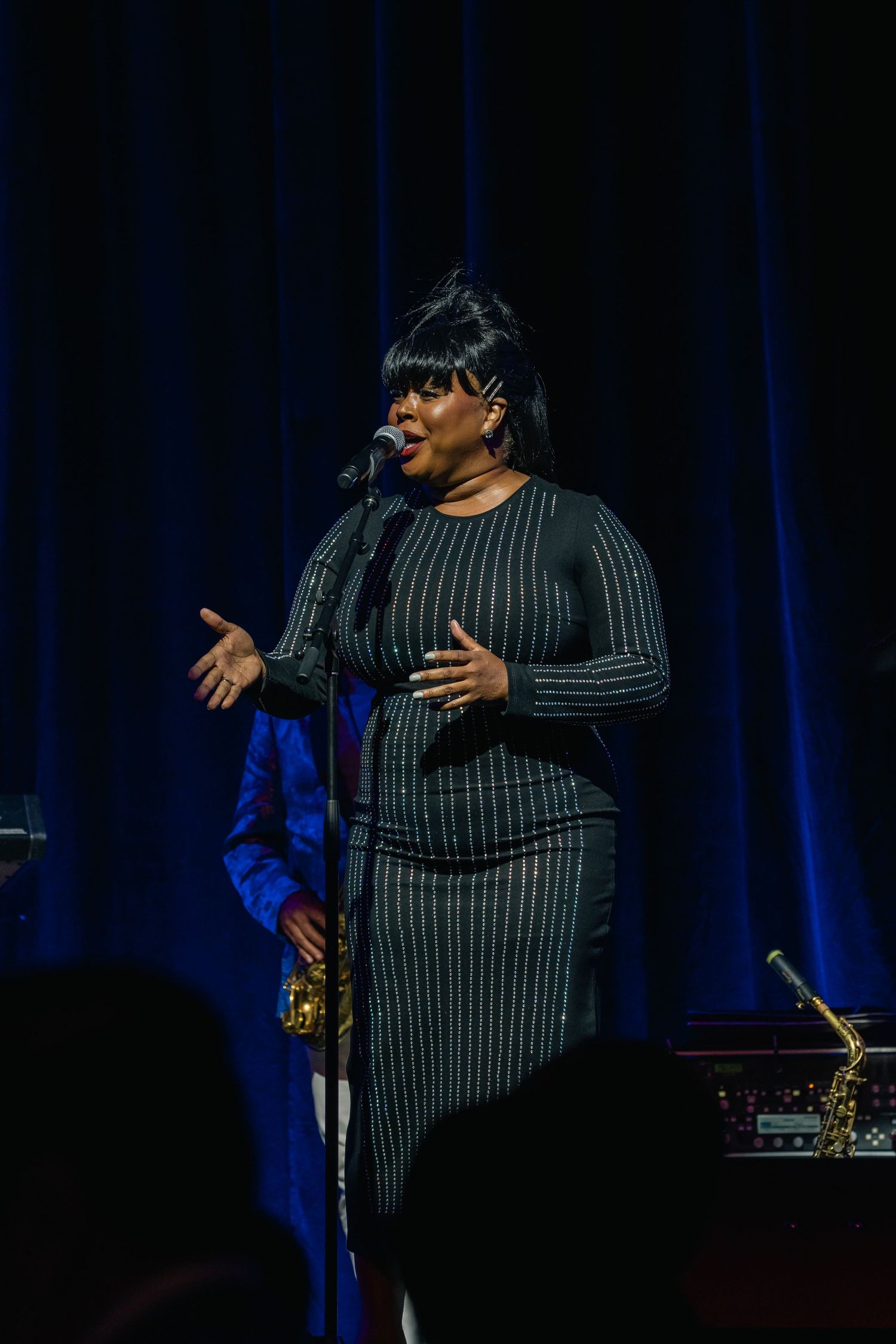 Singer performing on stage in striped outfit with dramatic lighting and microphone.