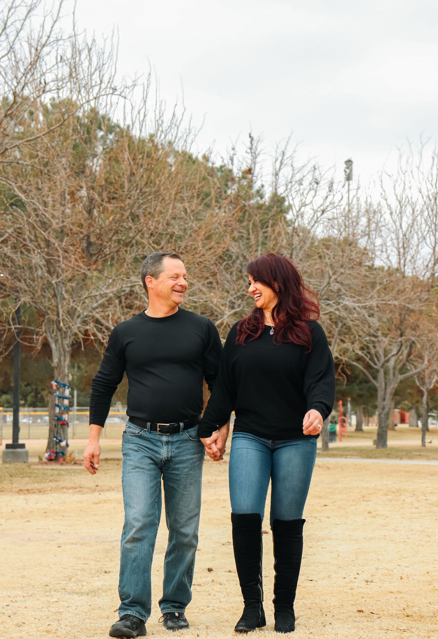 Couple holding hands and laughing while walking together in a park during winter.