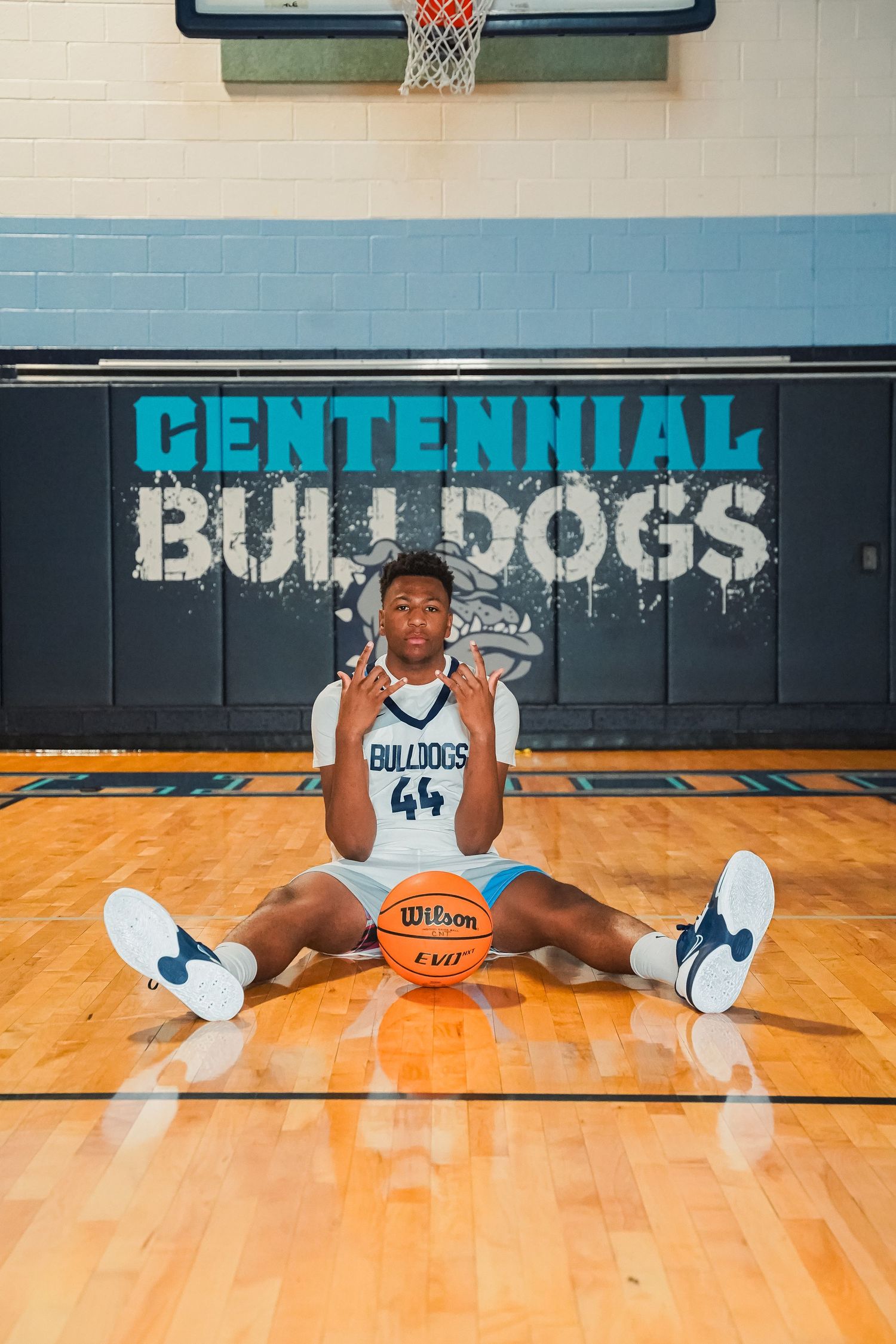 Basketball player performs splits stretch on hardwood court with Centennial Bulldogs signage.