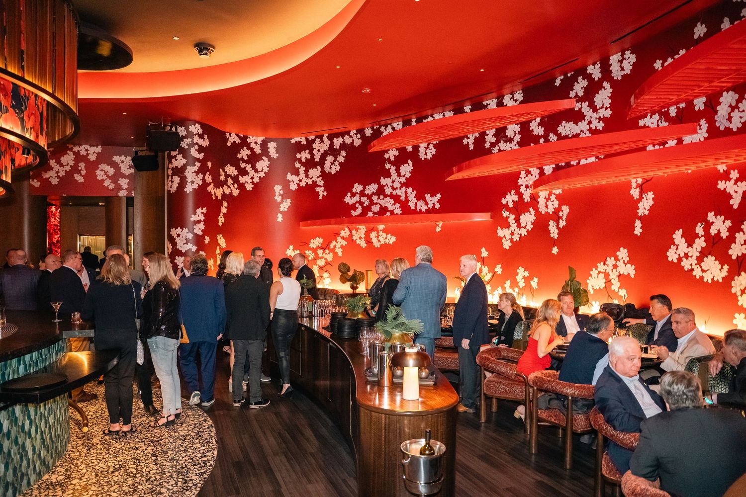 An elegant restaurant interior with red walls adorned with cherry blossom patterns and guests dining.