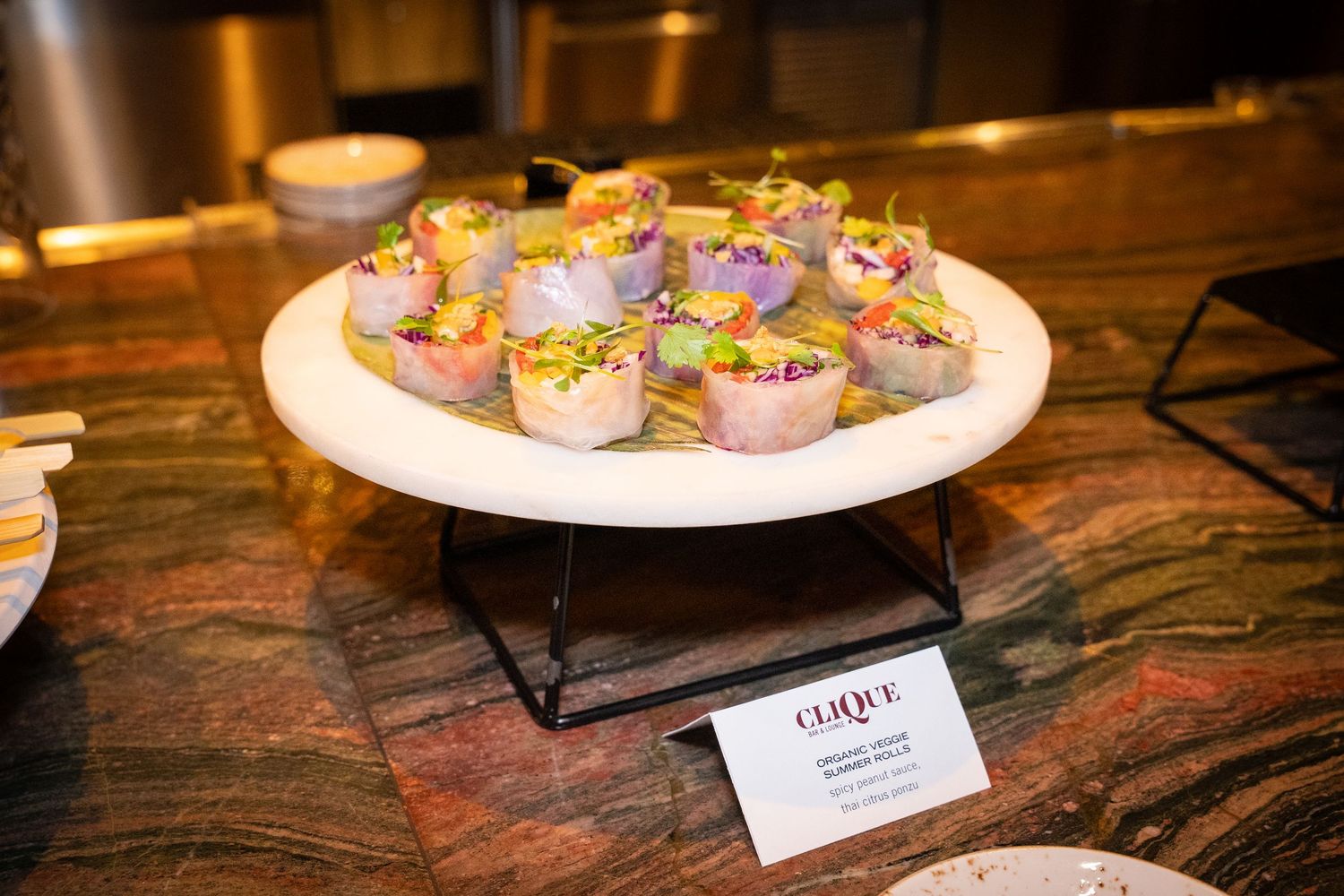 Elegant catered appetizers garnished with purple flowers displayed on white plate with description card.
