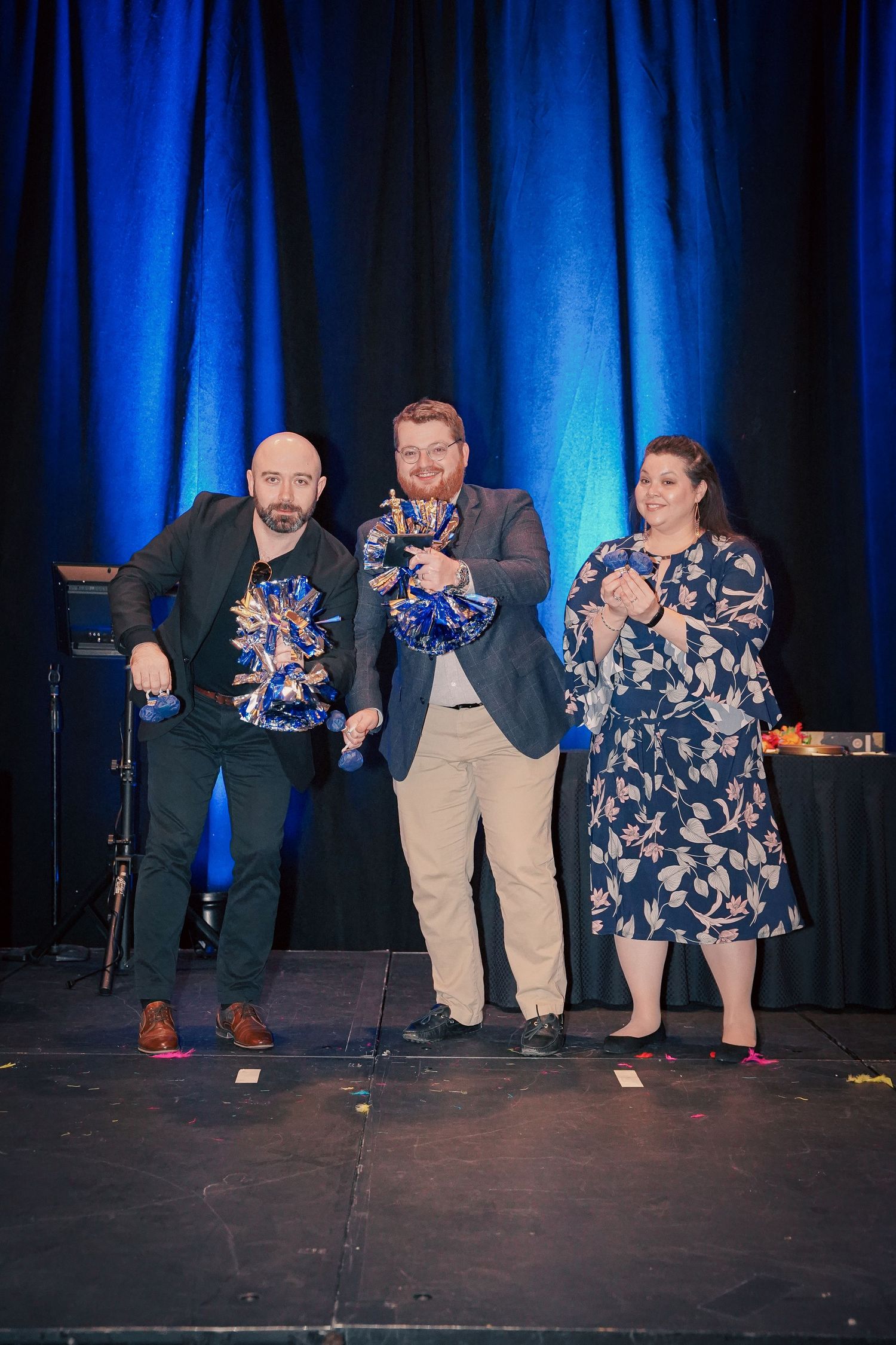 Three award recipients holding trophies on stage with blue lighting backdrop.
