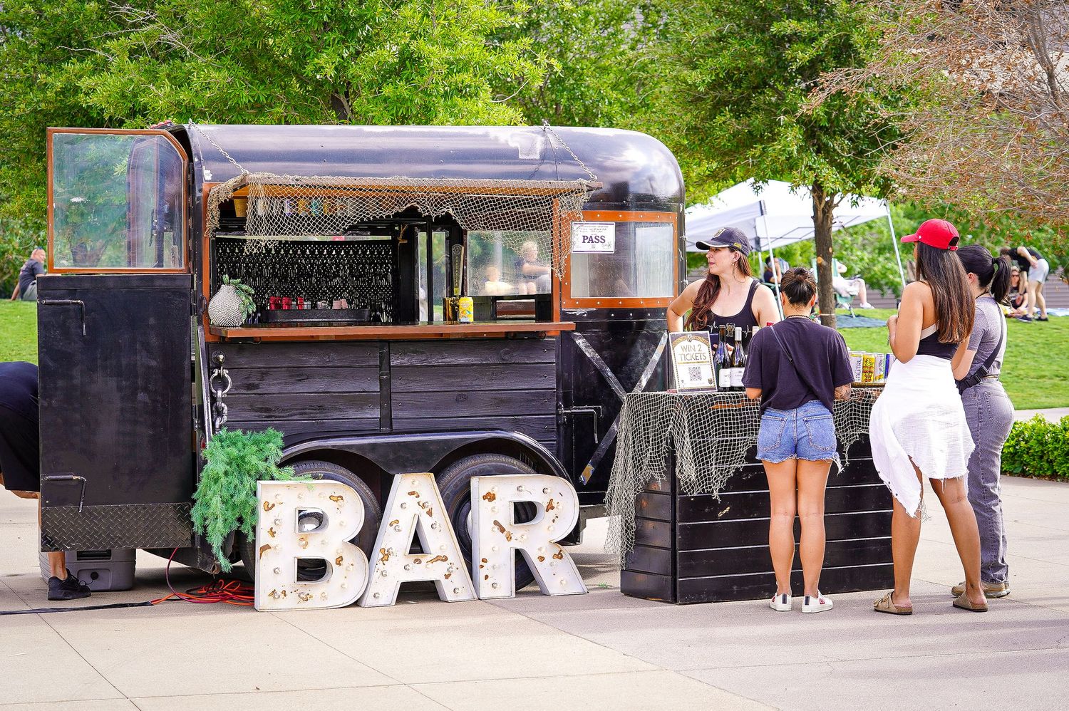 Mobile bar setup at outdoor event with decorative BAR sign and customers waiting in line.