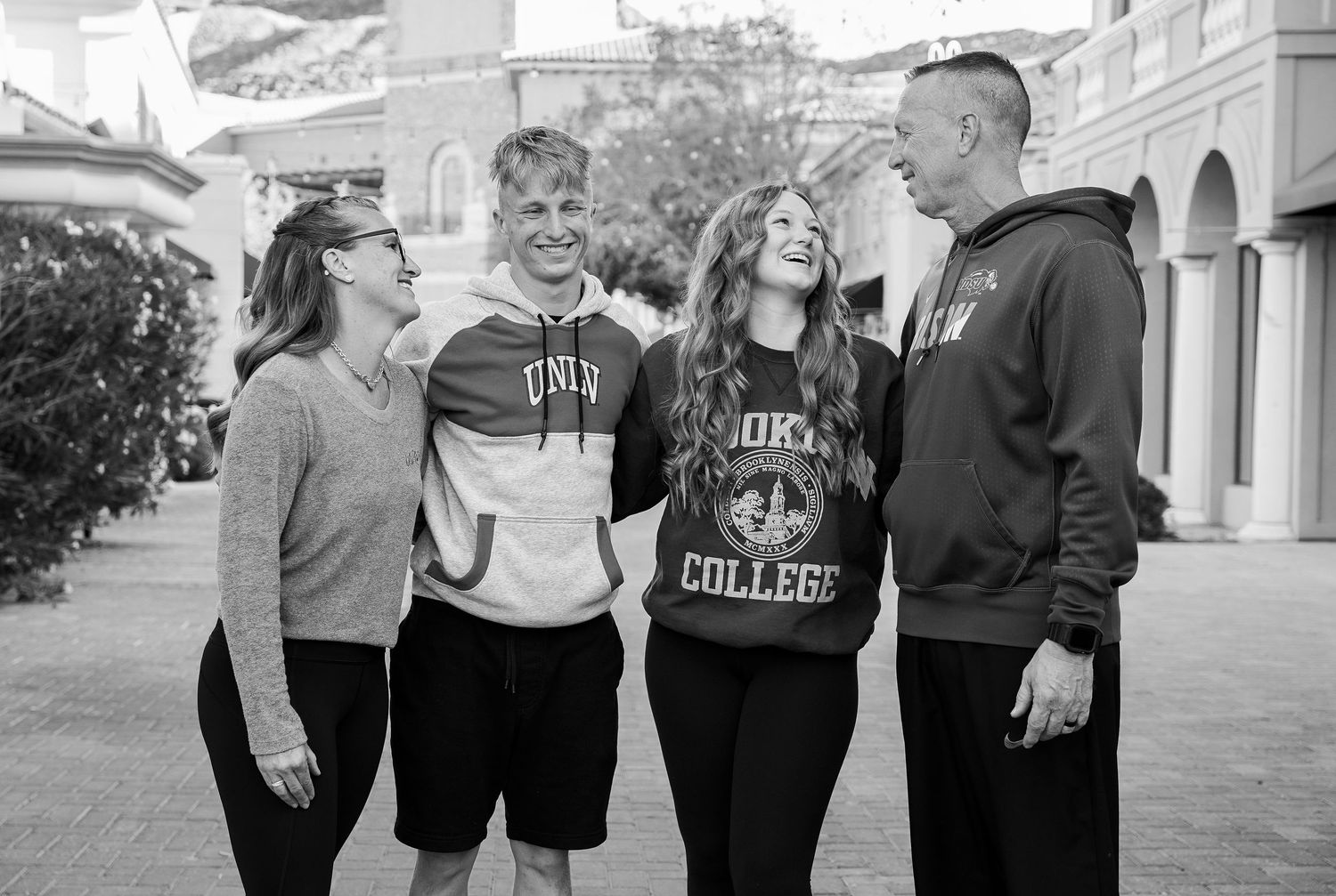 A black and white photo of college students wearing hoodies sharing a lighthearted moment together on campus.