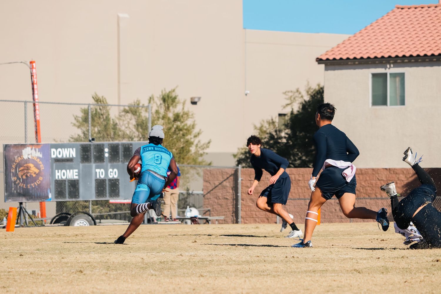 Athletes in turquoise uniforms training on a dry grass field during a sunny day.