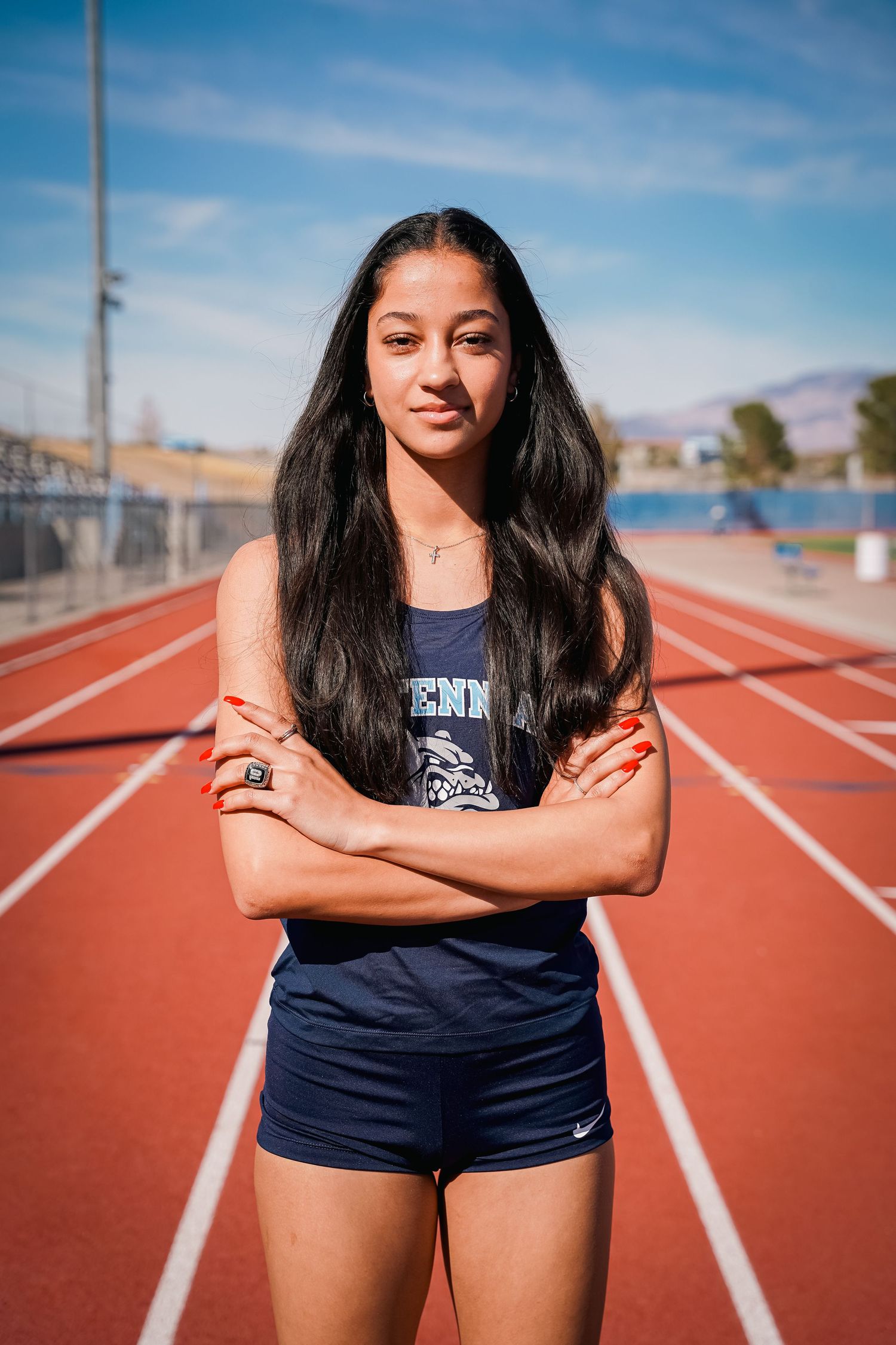 Athletic person standing confidently on a red running track wearing navy sports attire.
