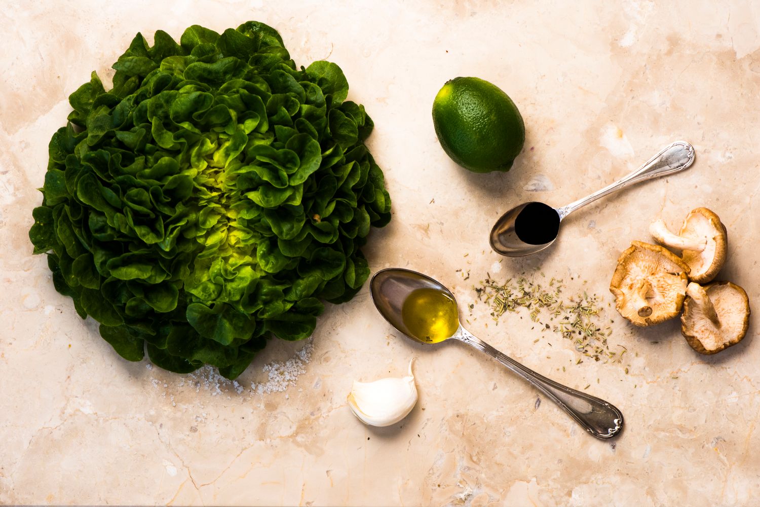 Fresh green butter lettuce head with lime, olive oil, garlic and spices arranged on light textured surface.