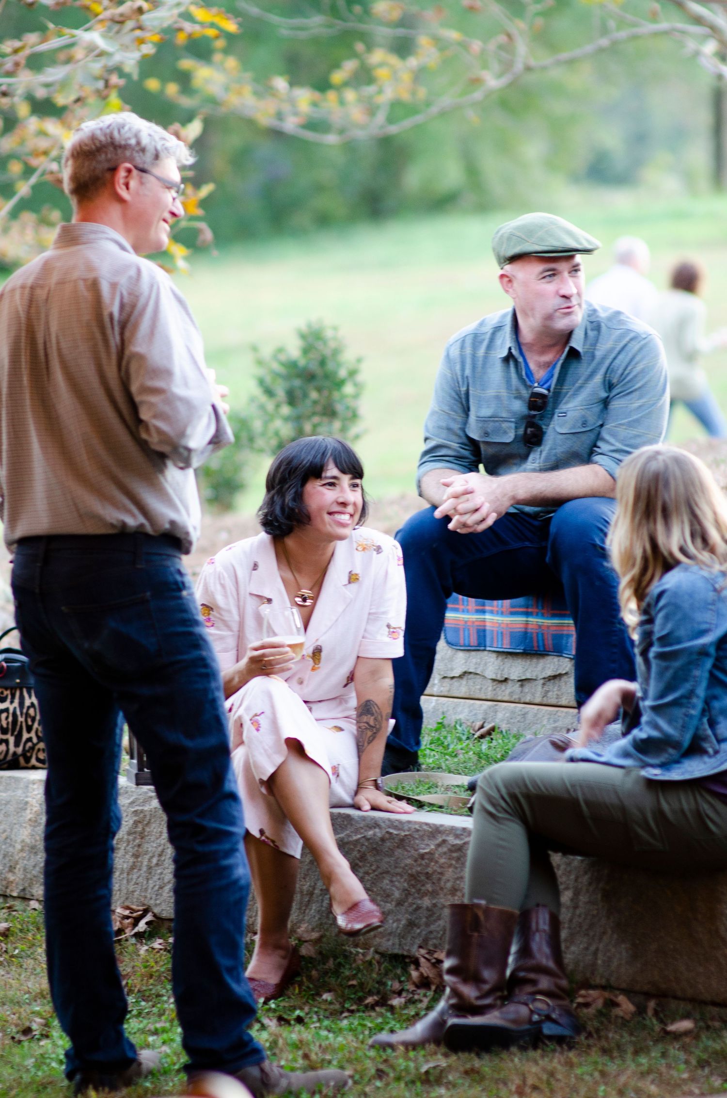 A group of people enjoying casual conversation while sitting and standing outdoors on a sunny autumn day.