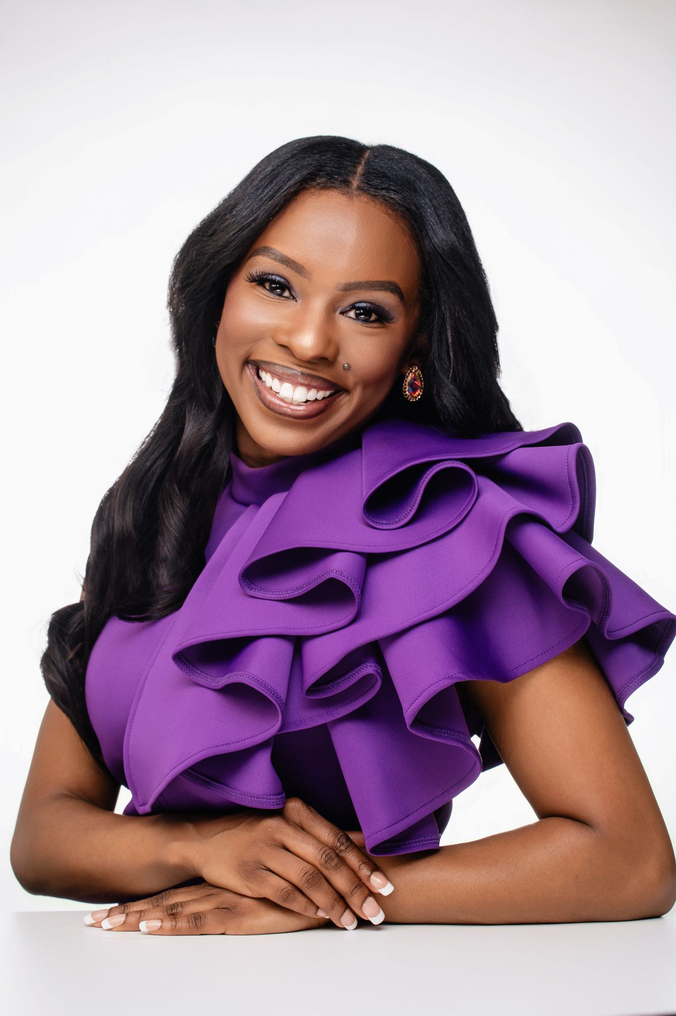 Professional studio portrait featuring a vibrant purple ruffled top against a light gray background.