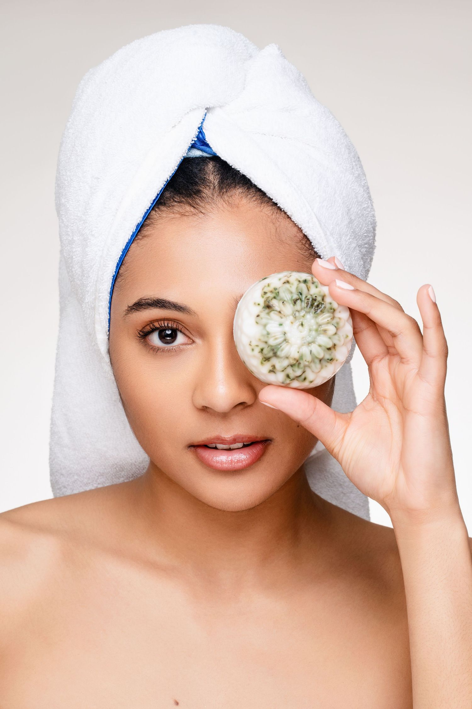 Beauty spa portrait of someone with a white towel on head holding a cucumber slice over one eye.