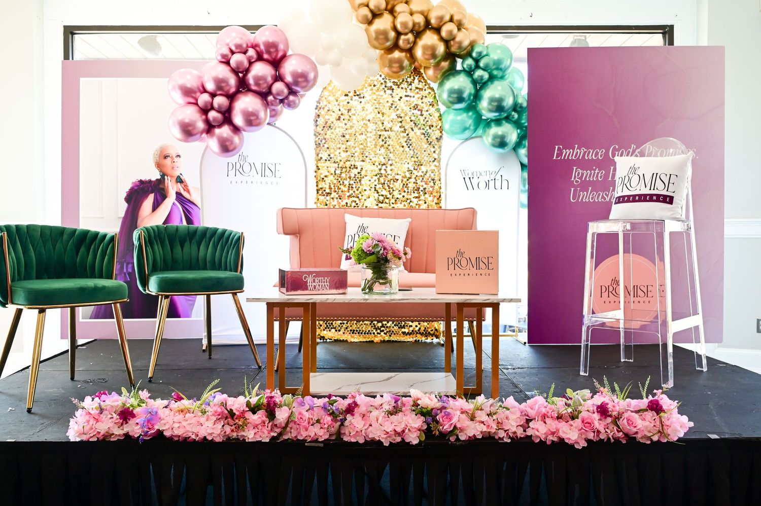 Luxurious event setup with emerald velvet chairs, gold sequin backdrop, colorful pom poms and pink floral arrangements.