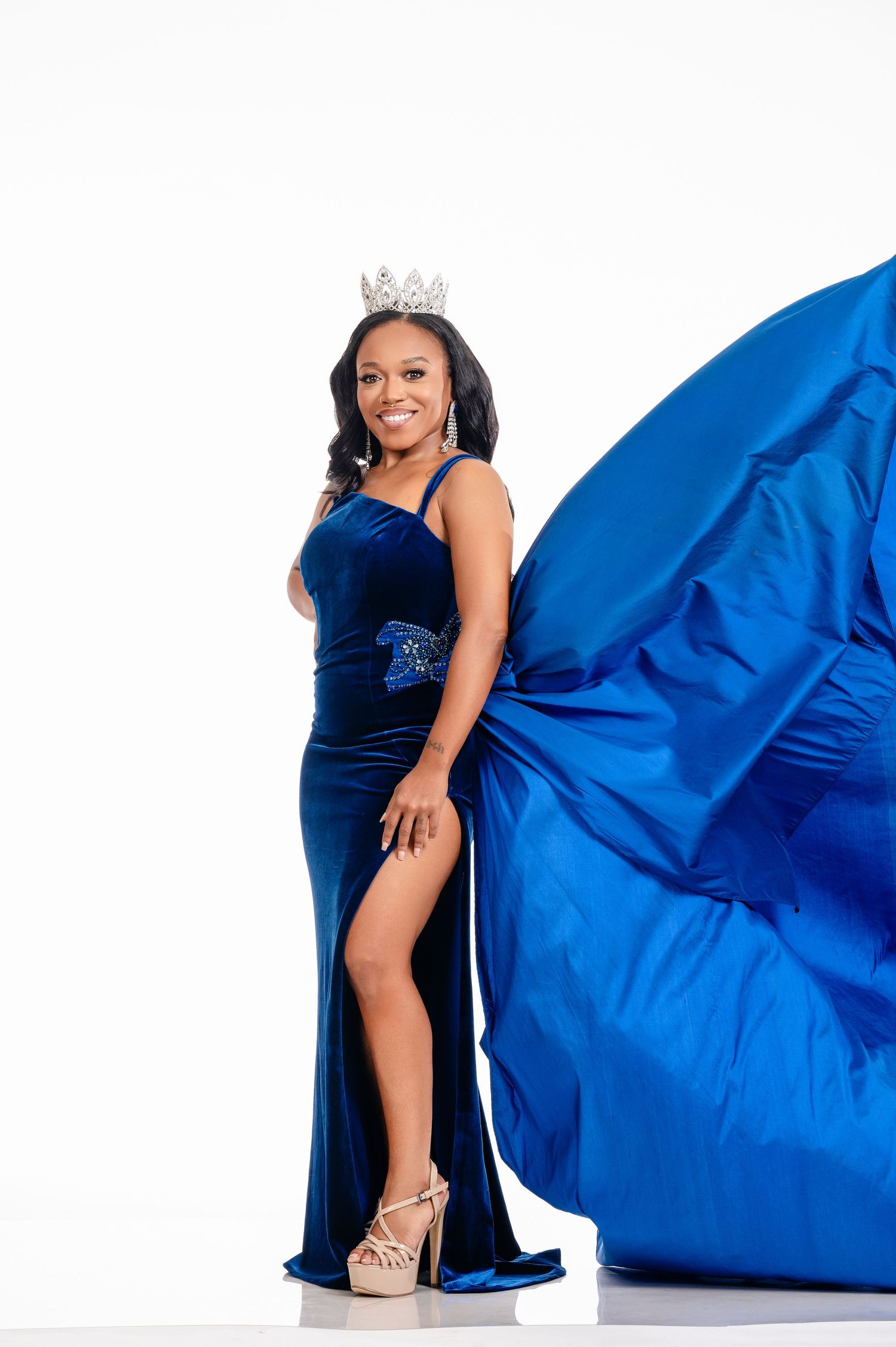 A glamorous photoshoot featuring a flowing royal blue gown against a white backdrop with elegant poses.