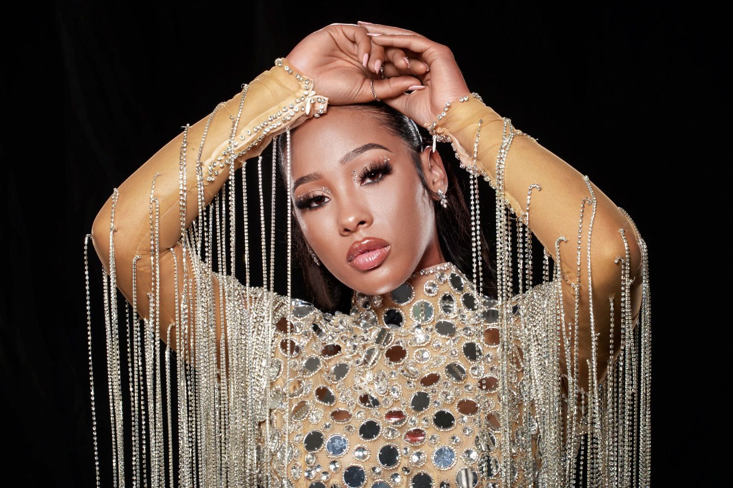 Elegant portrait with beaded silver jewelry chains draping down from a shimmering embellished high-neck top against dark background.