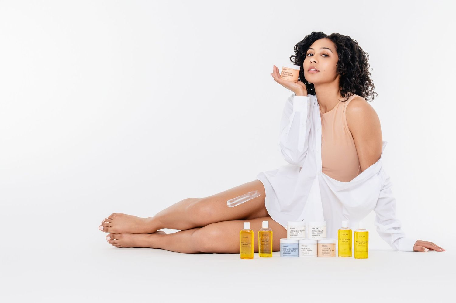 Person in white robe relaxing with beauty products and essential oils on white background.