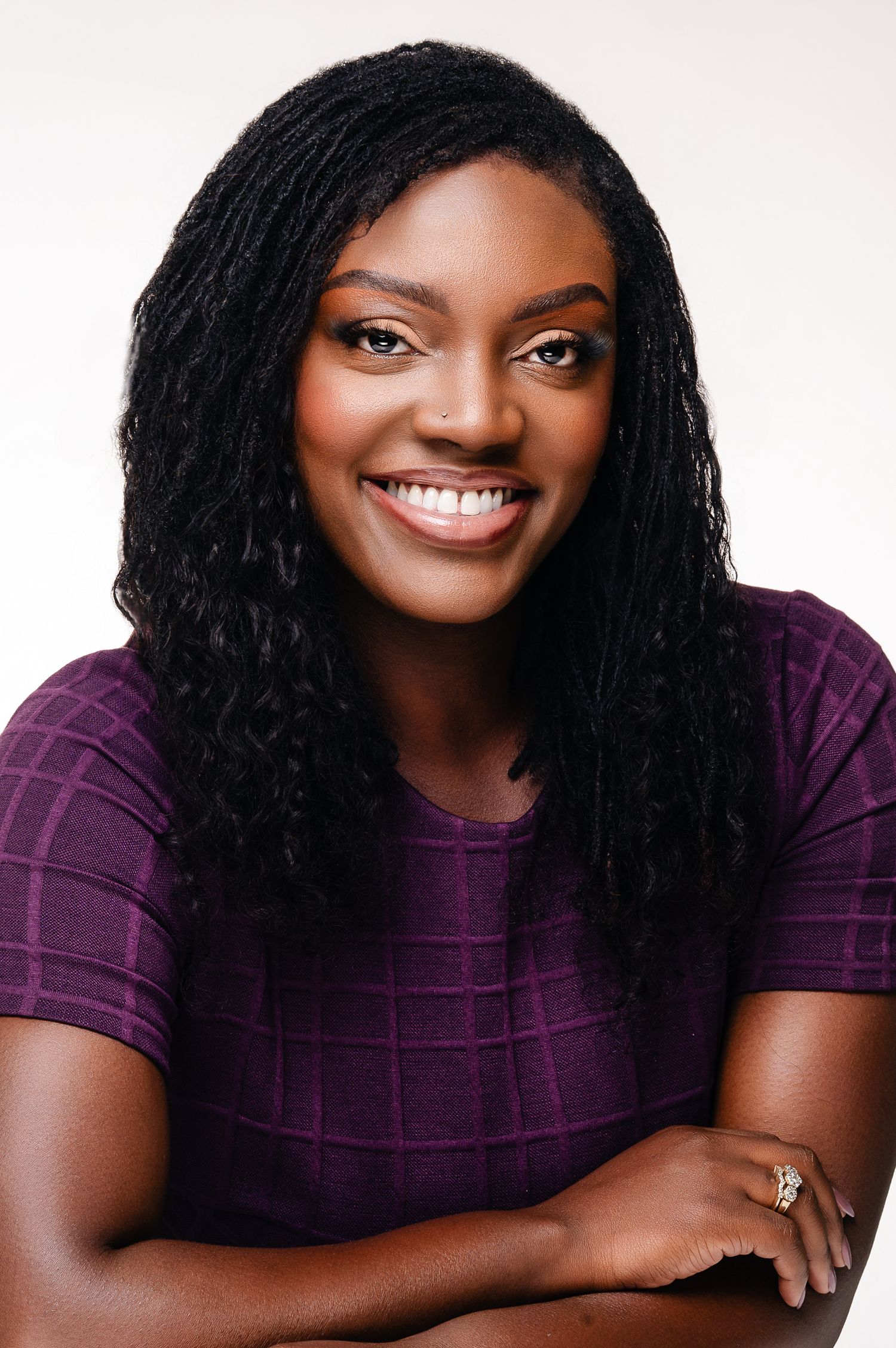 Woman in purple top smiling warmly in professional headshot series against white background.