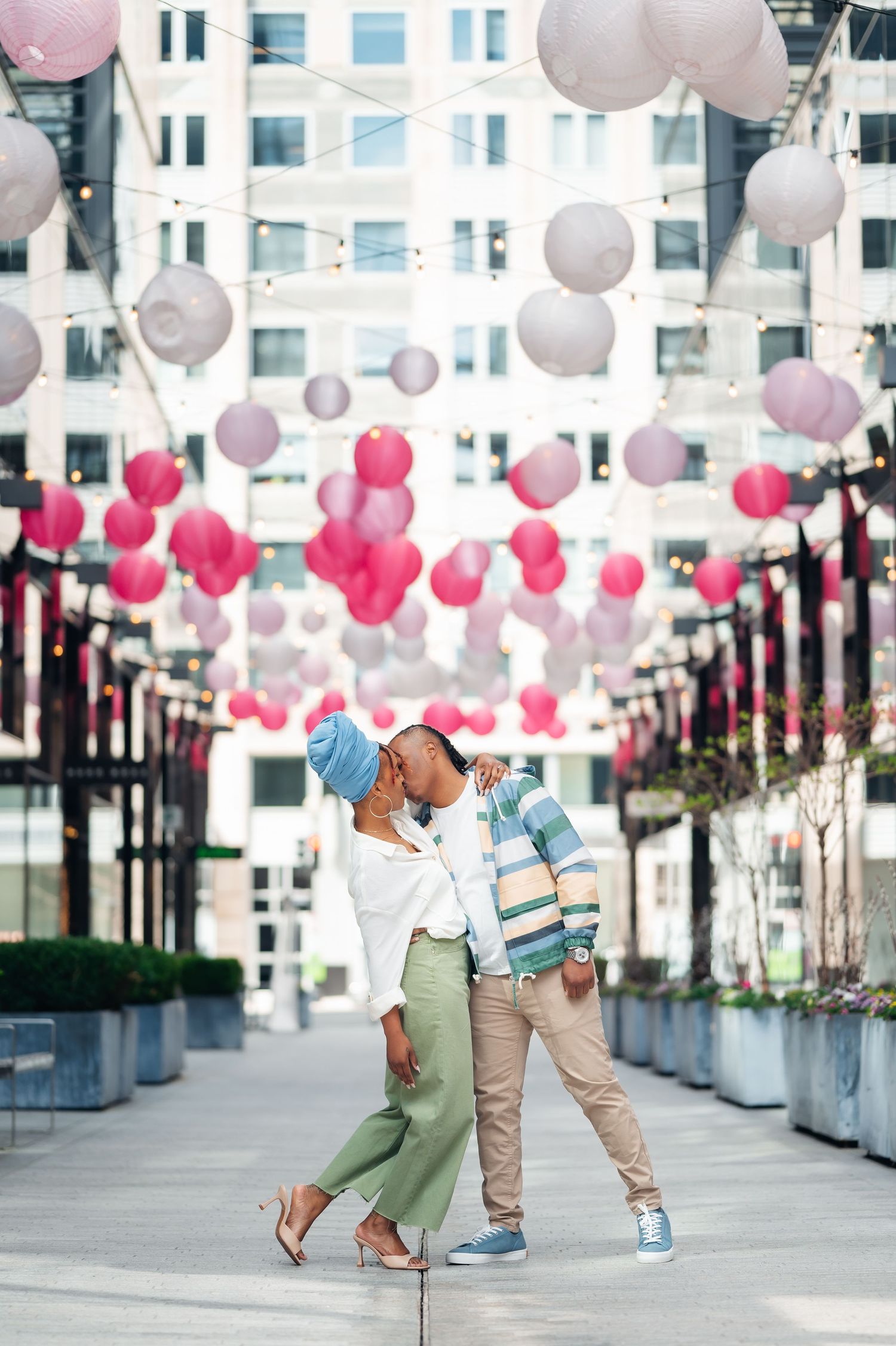 A romantic scene under pink and white balloon decor in an urban setting with modern buildings in the background.