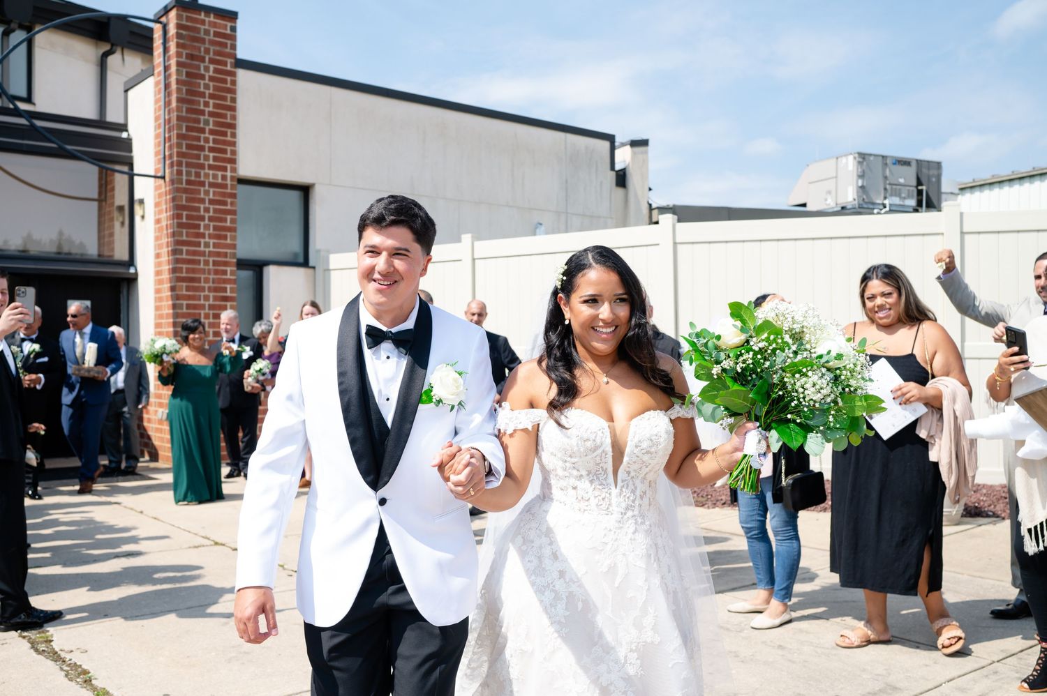 Newlyweds walk arm in arm while exiting their wedding ceremony as guests look on and celebrate.