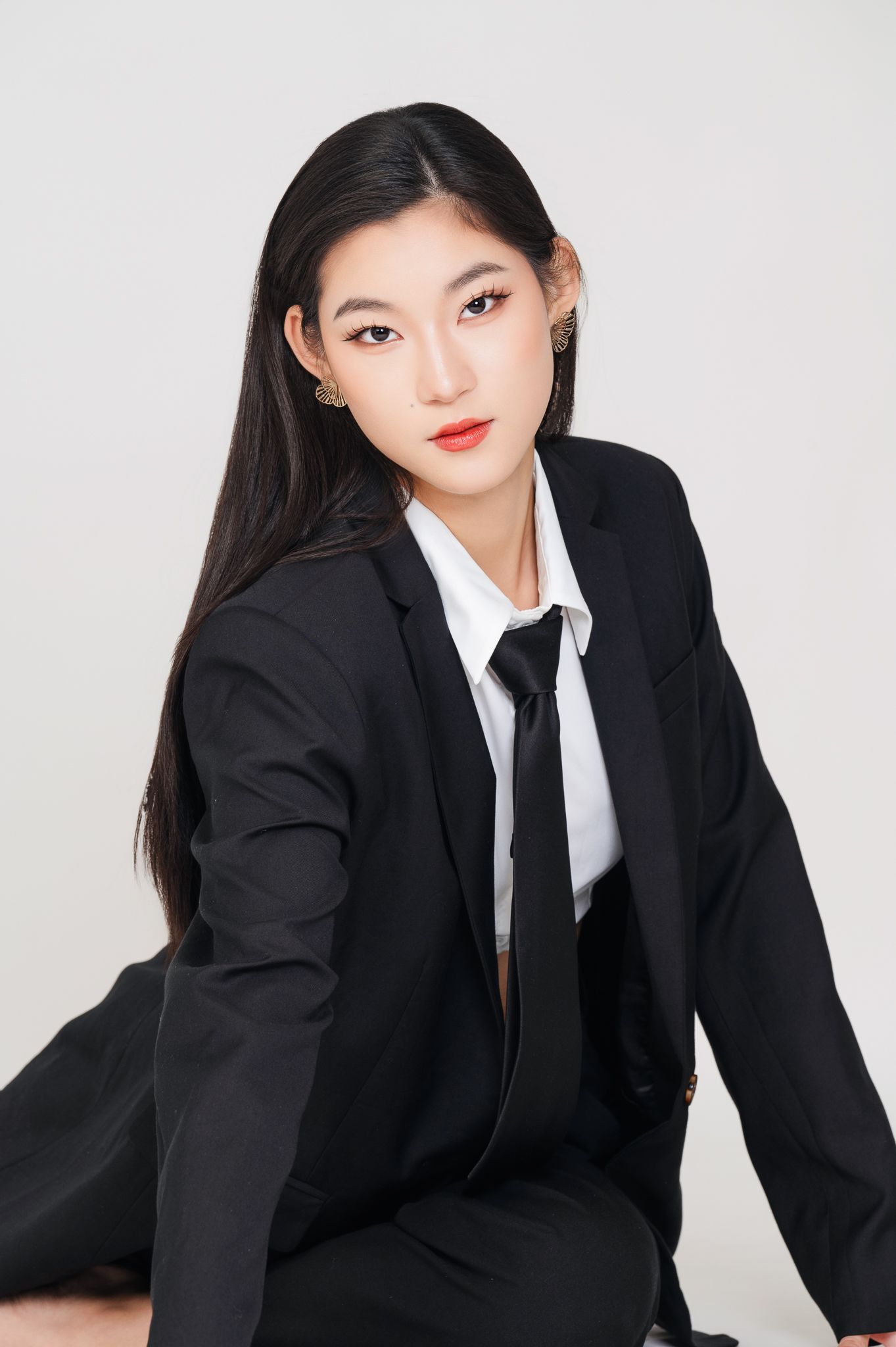 Professional portrait in black suit and tie with minimalist white background.