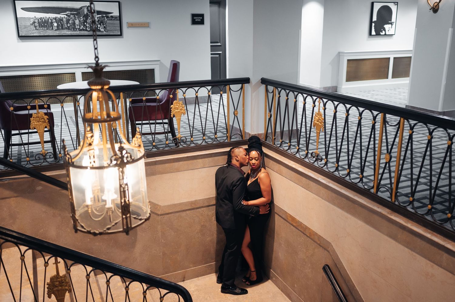 Elegant chandelier hangs above a curved staircase with ornate iron railings in a luxurious interior space.