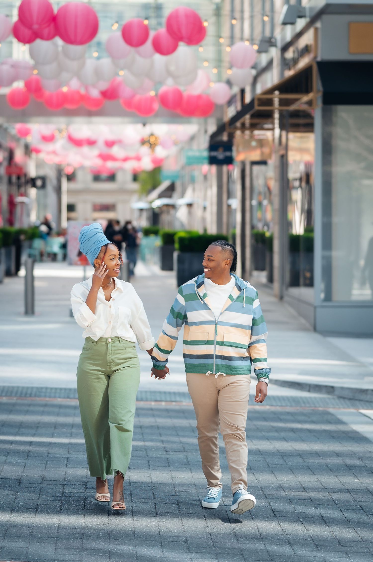Couple walking down a modern street decorated with pink lanterns as they share a romantic moment together.