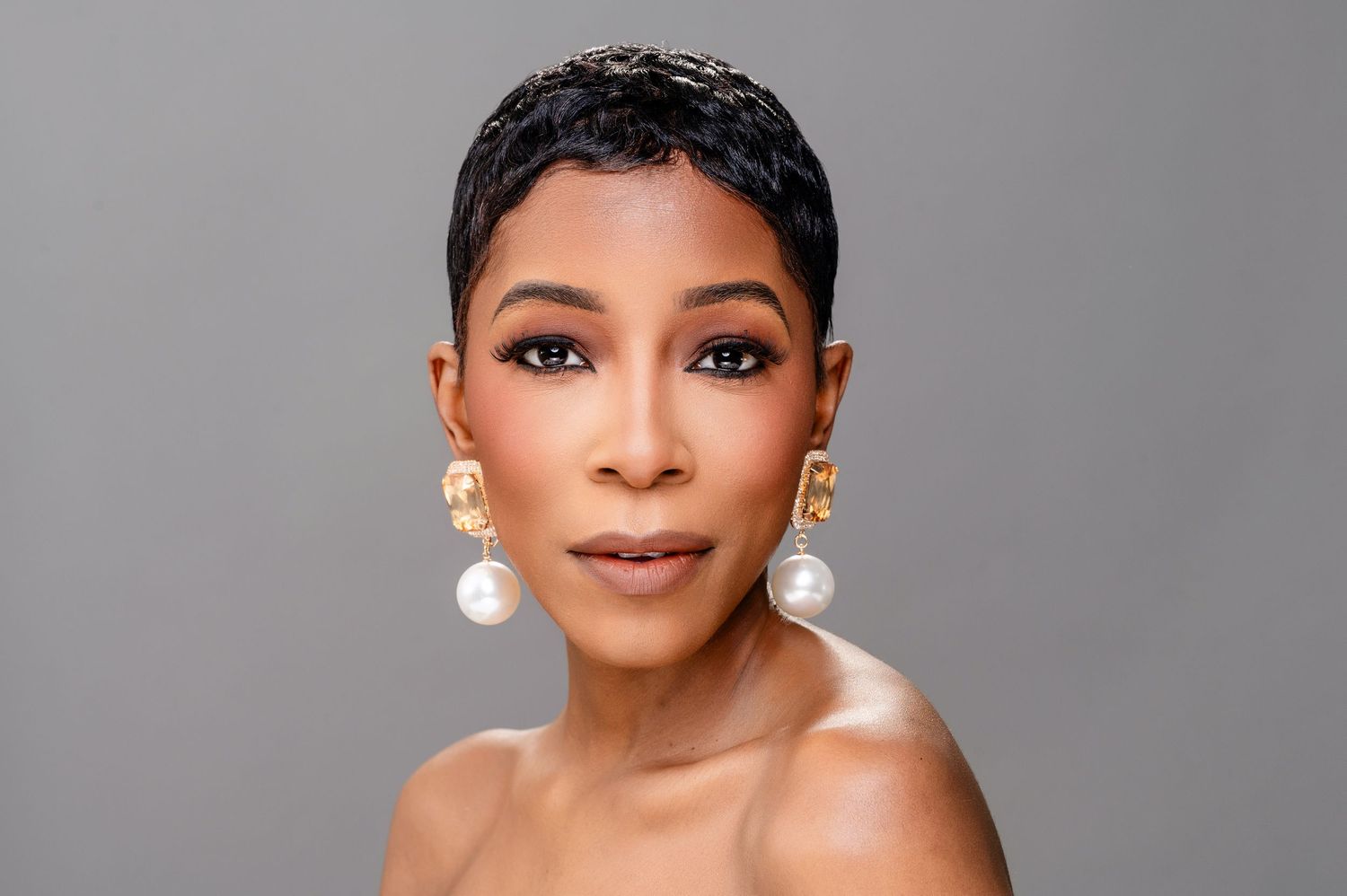 A glamorous portrait series showing elegant makeup, pearl earrings and bare shoulders against a gray backdrop.